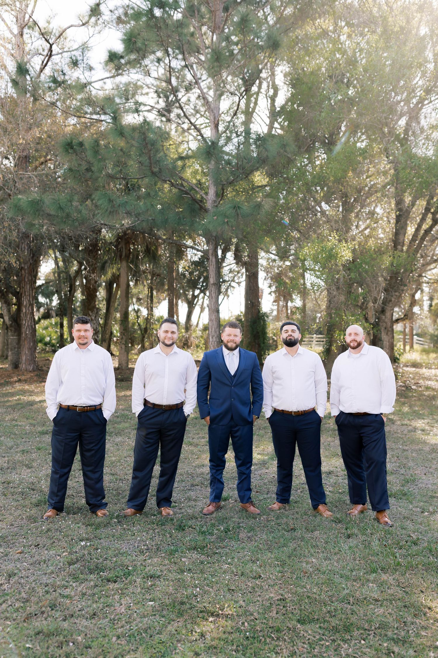 Groomsmen in navy suits and white shirts pose together on a grassy hill.