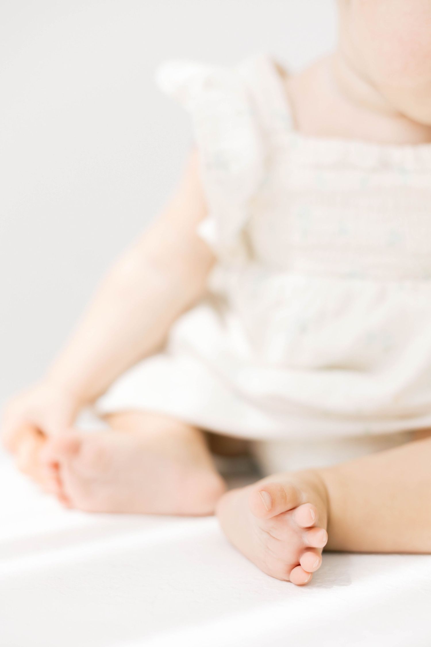 Close-up of baby feet on white bedding in soft natural light.