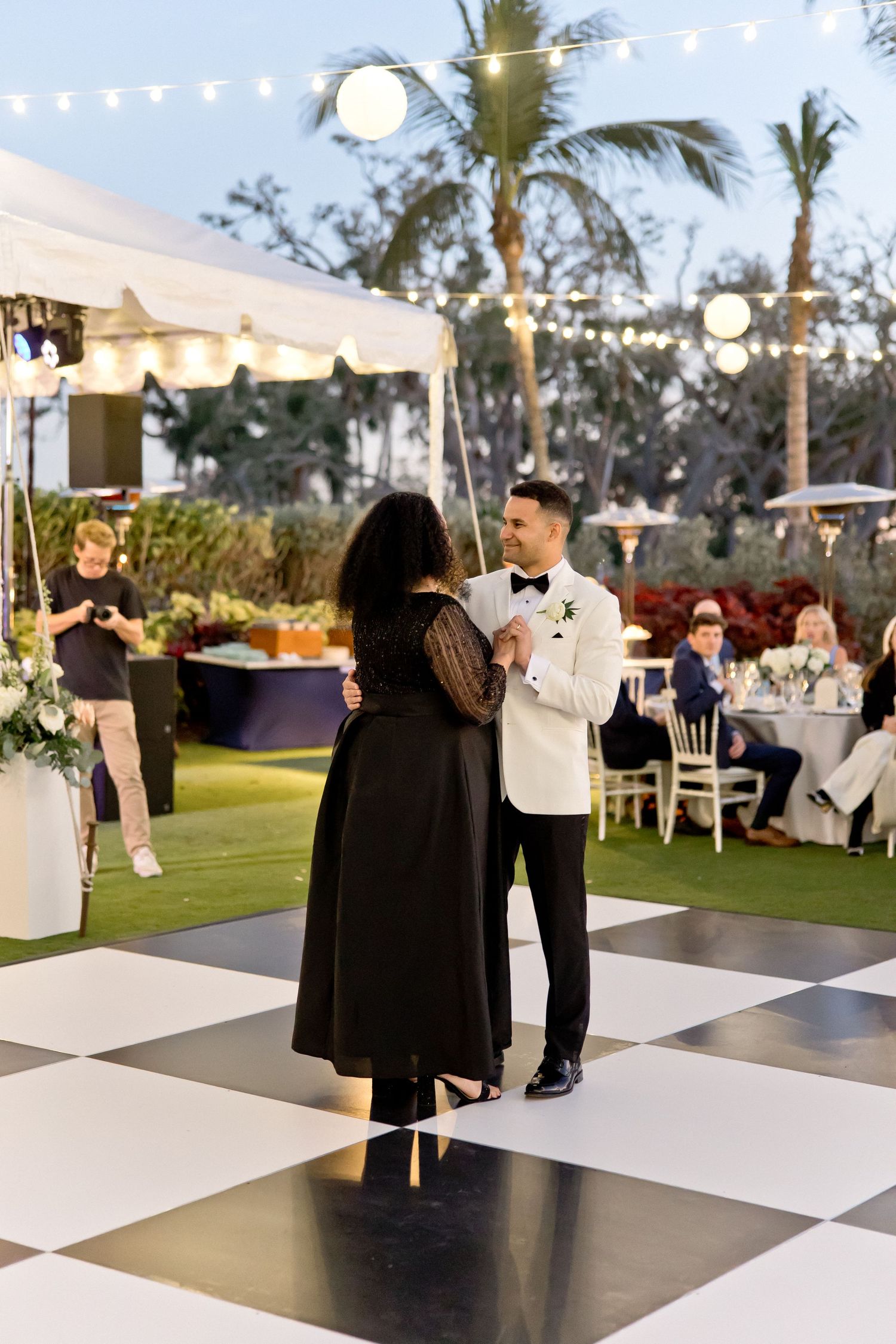 Guests dancing on a black and white checkered dance floor at an outdoor evening reception.