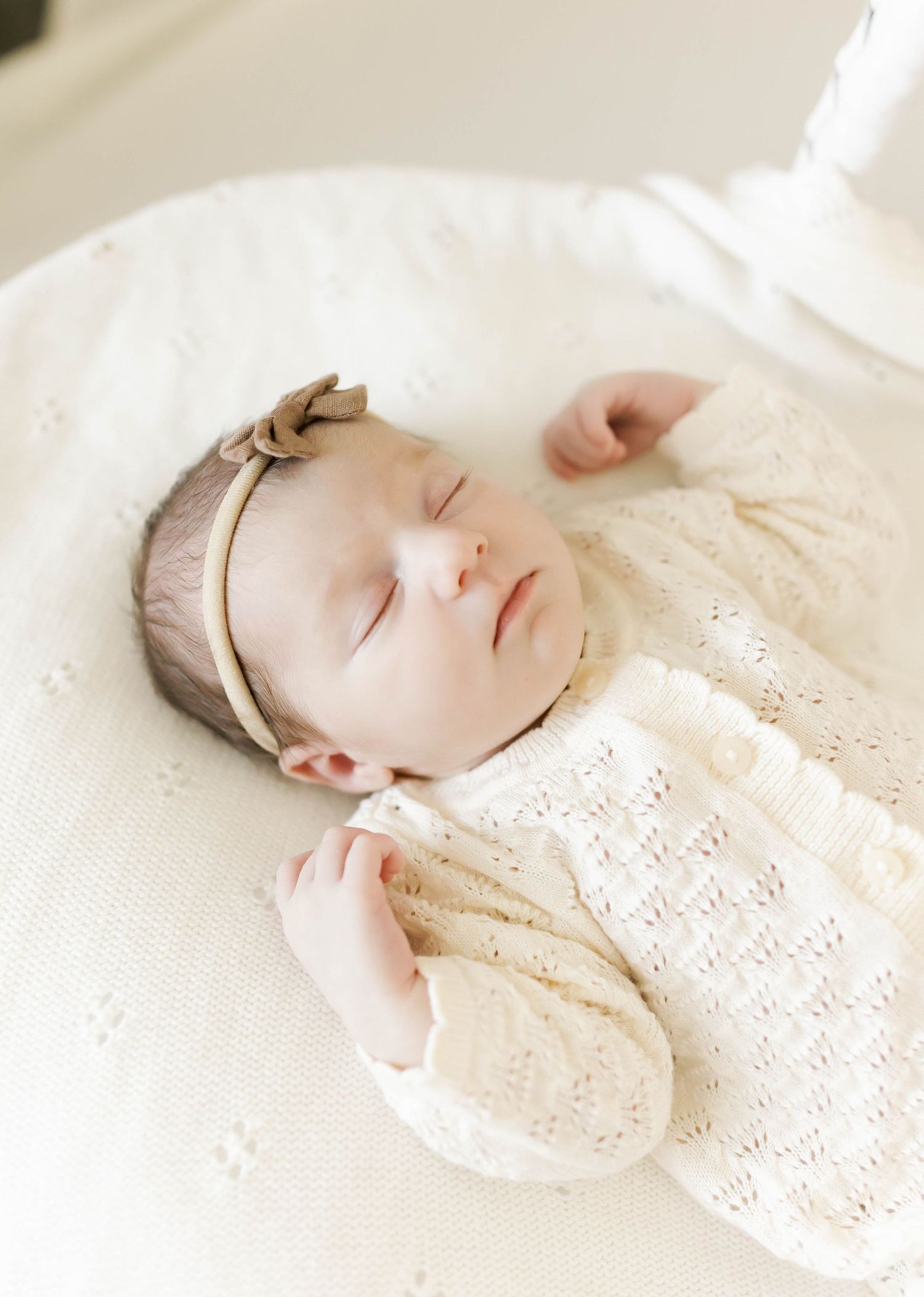 Peaceful newborn in cream lace outfit sleeping on white textured bedding.
