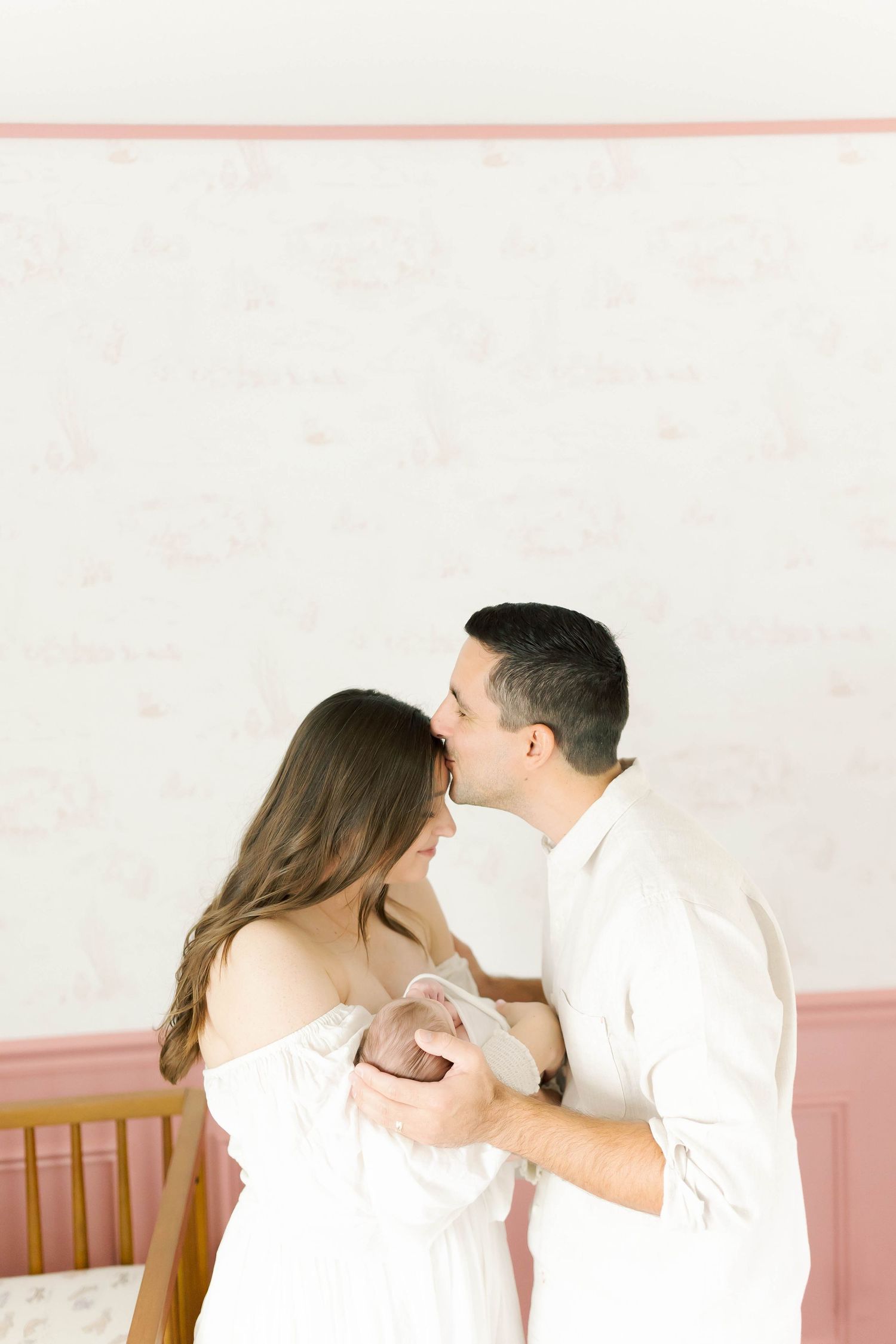 A tender moment between a couple in white clothing sharing an intimate embrace in a nursery.