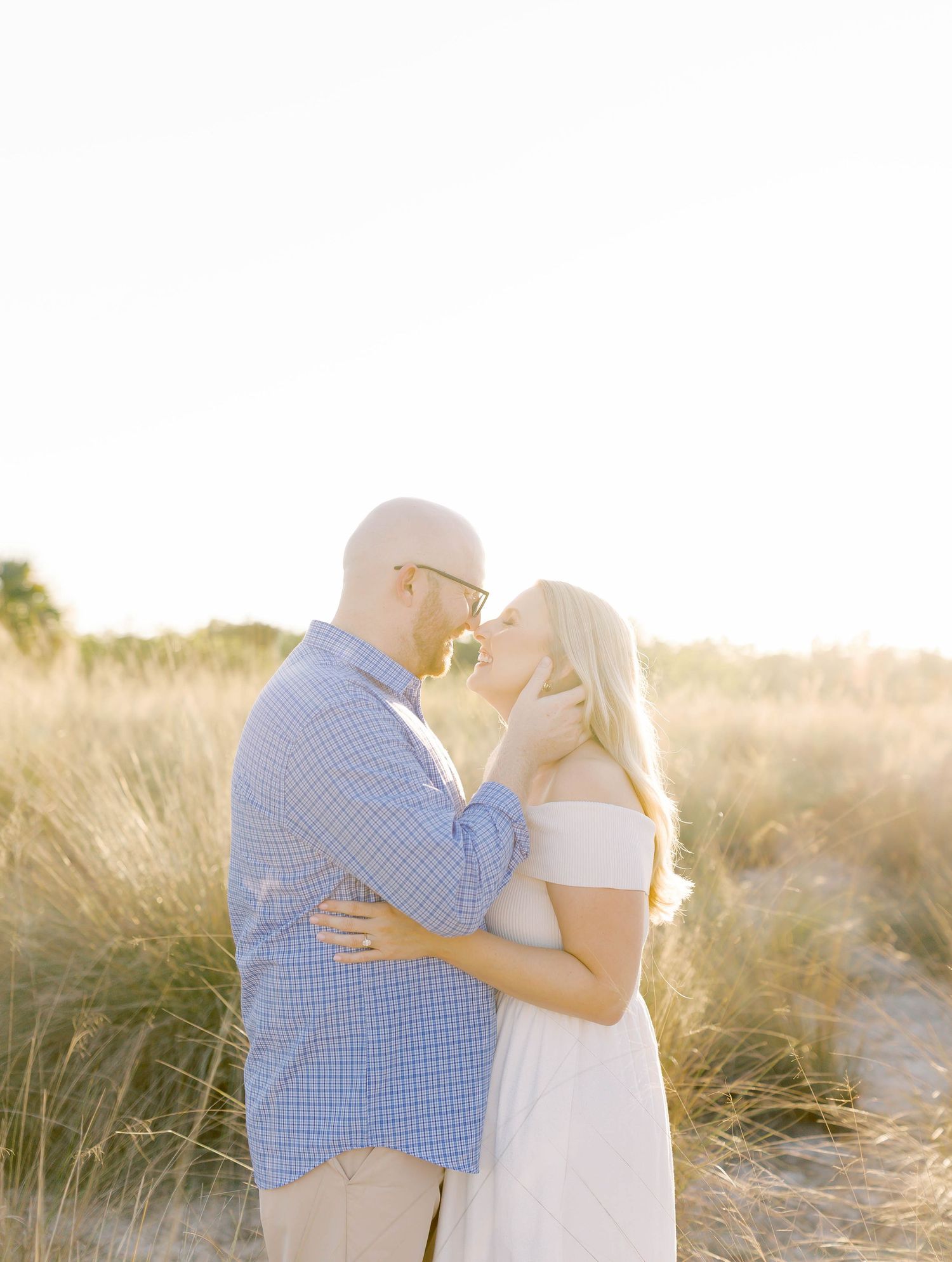Couple embracing in soft golden light among tall grass during sunset photoshoot.