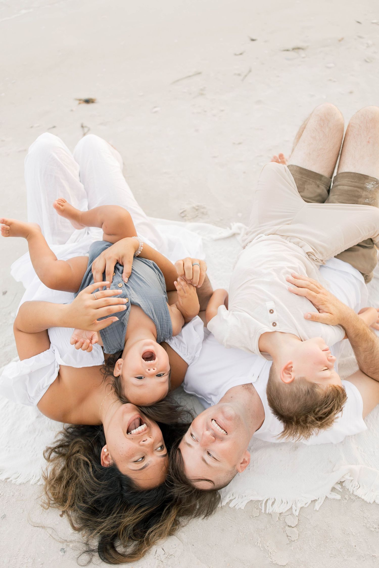 Family lying together on a white blanket at the beach sharing joyful moments.