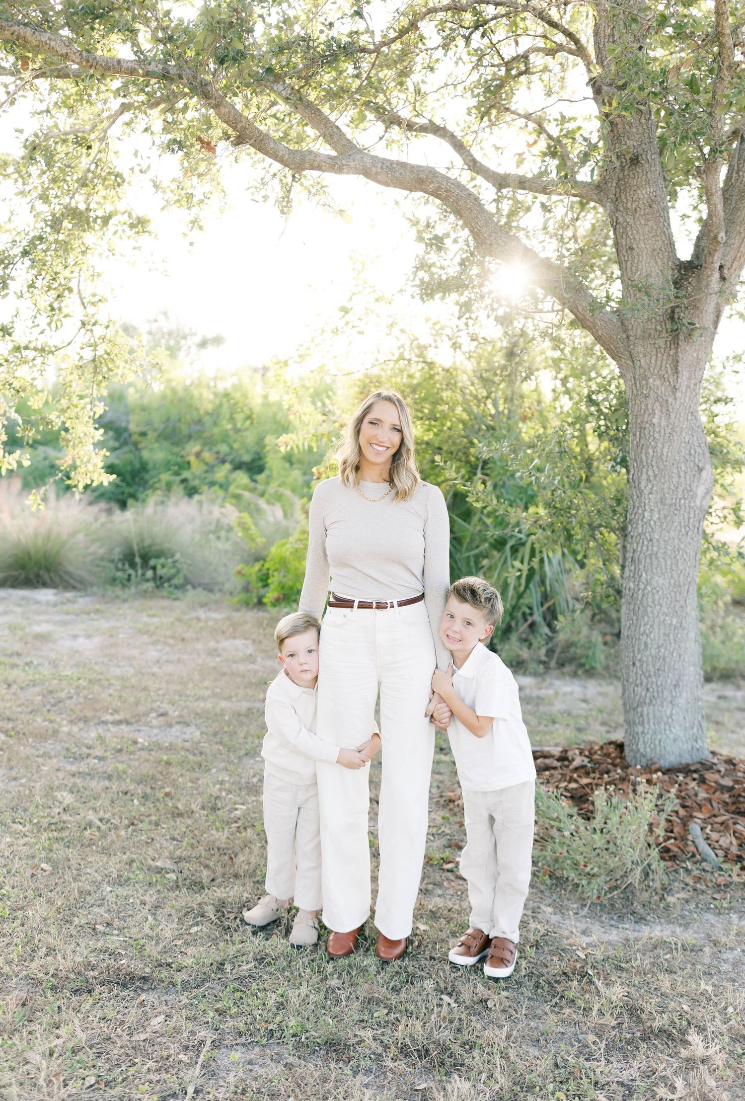 Family wearing coordinated white outfits poses together under a large oak tree.
