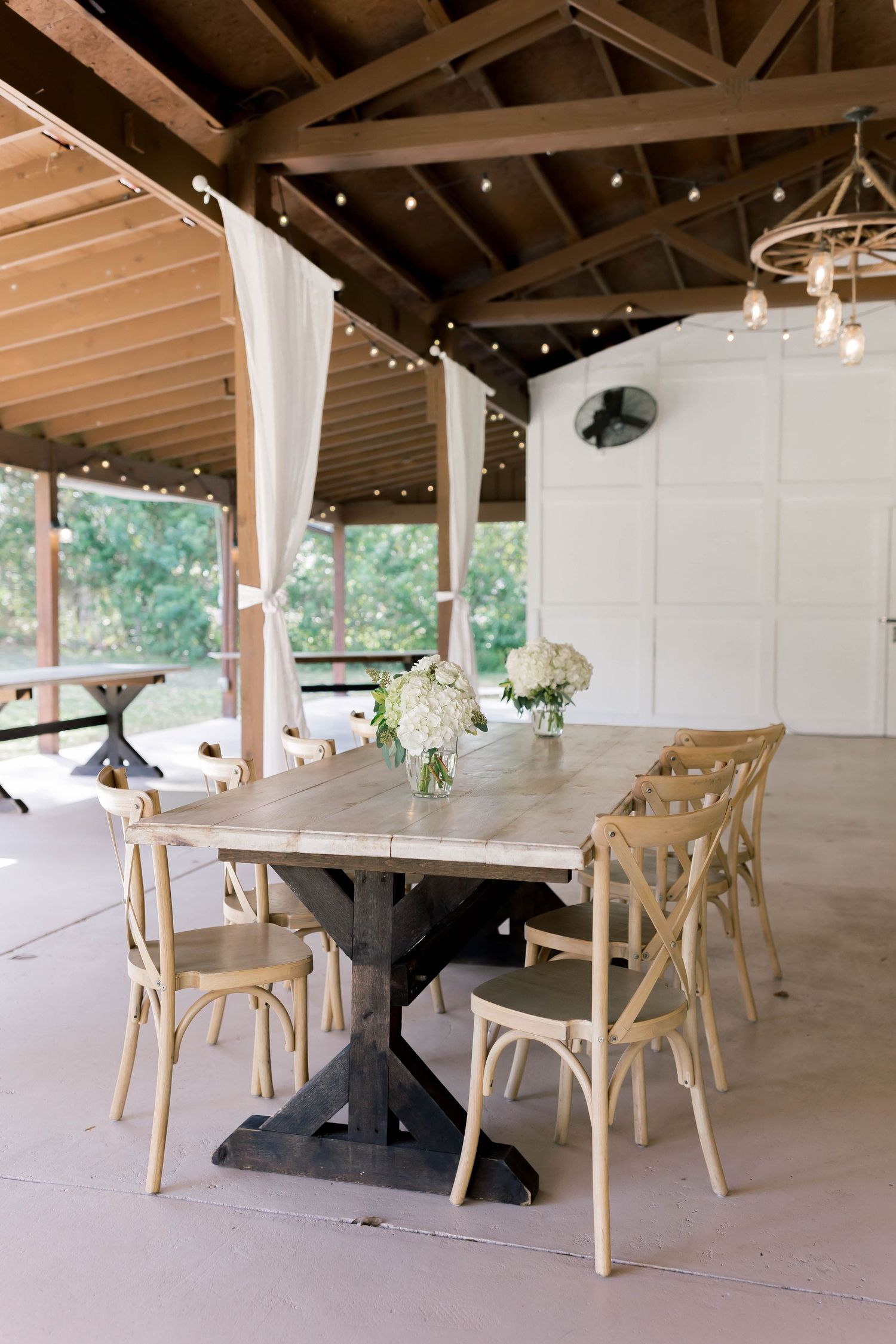 Modern rustic reception venue with wooden beams and cross-back chairs set for a wedding celebration.
