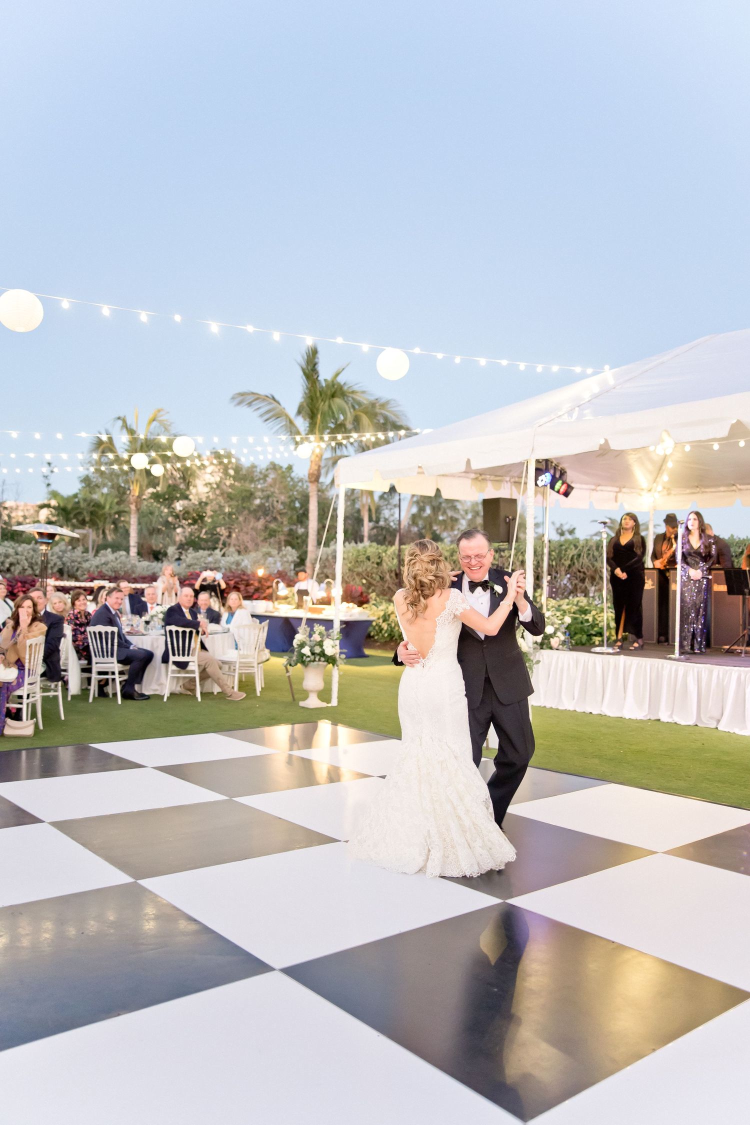 Wedding reception dance sequence on a black and white checkered floor under string lights and palm trees.