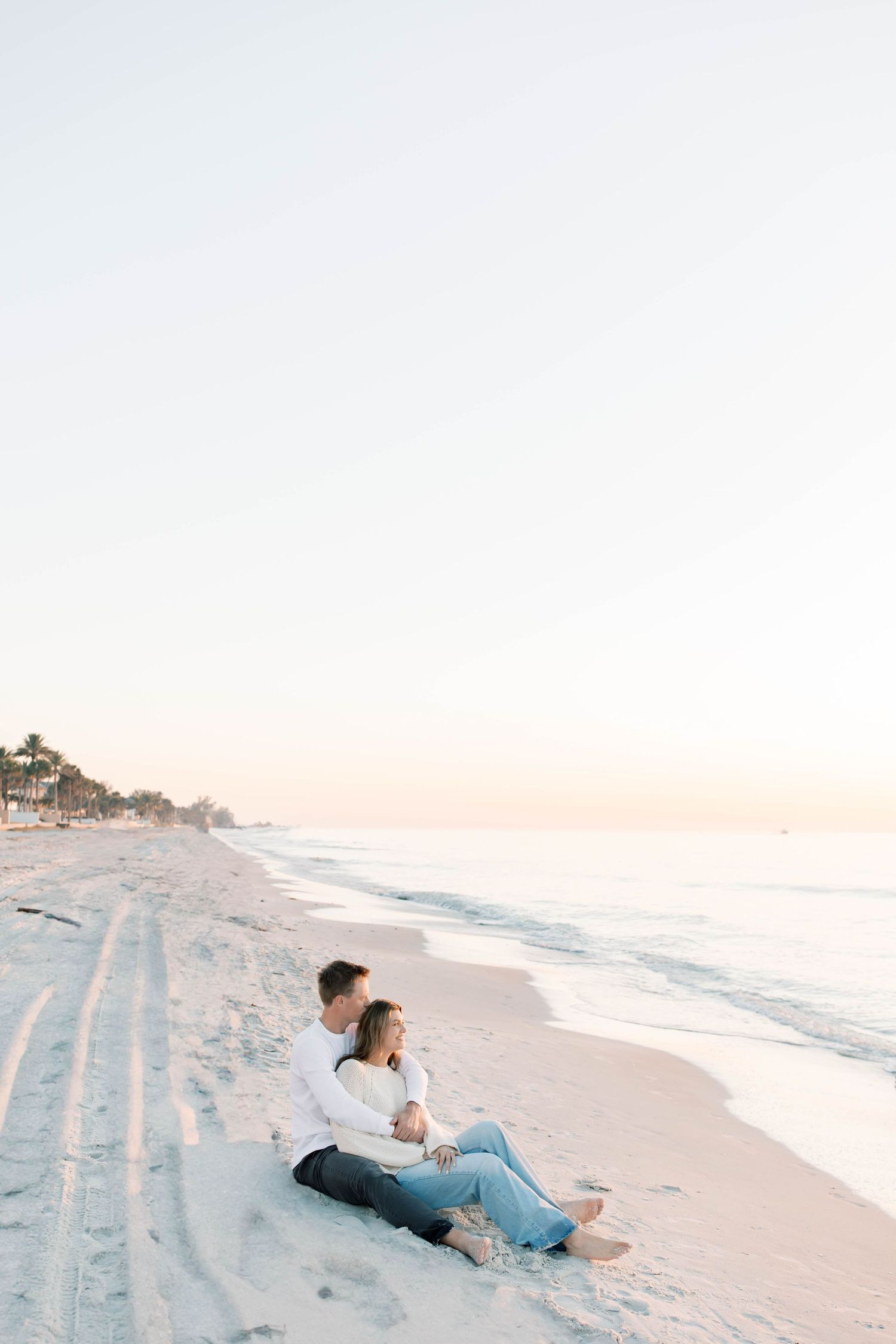 Two people relax on a pristine beach during golden hour with waves in the background.