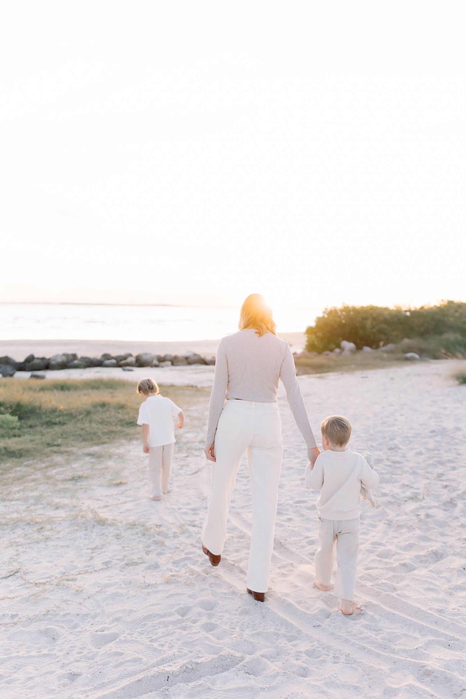 Family in white clothing walks along sandy beach during golden hour.