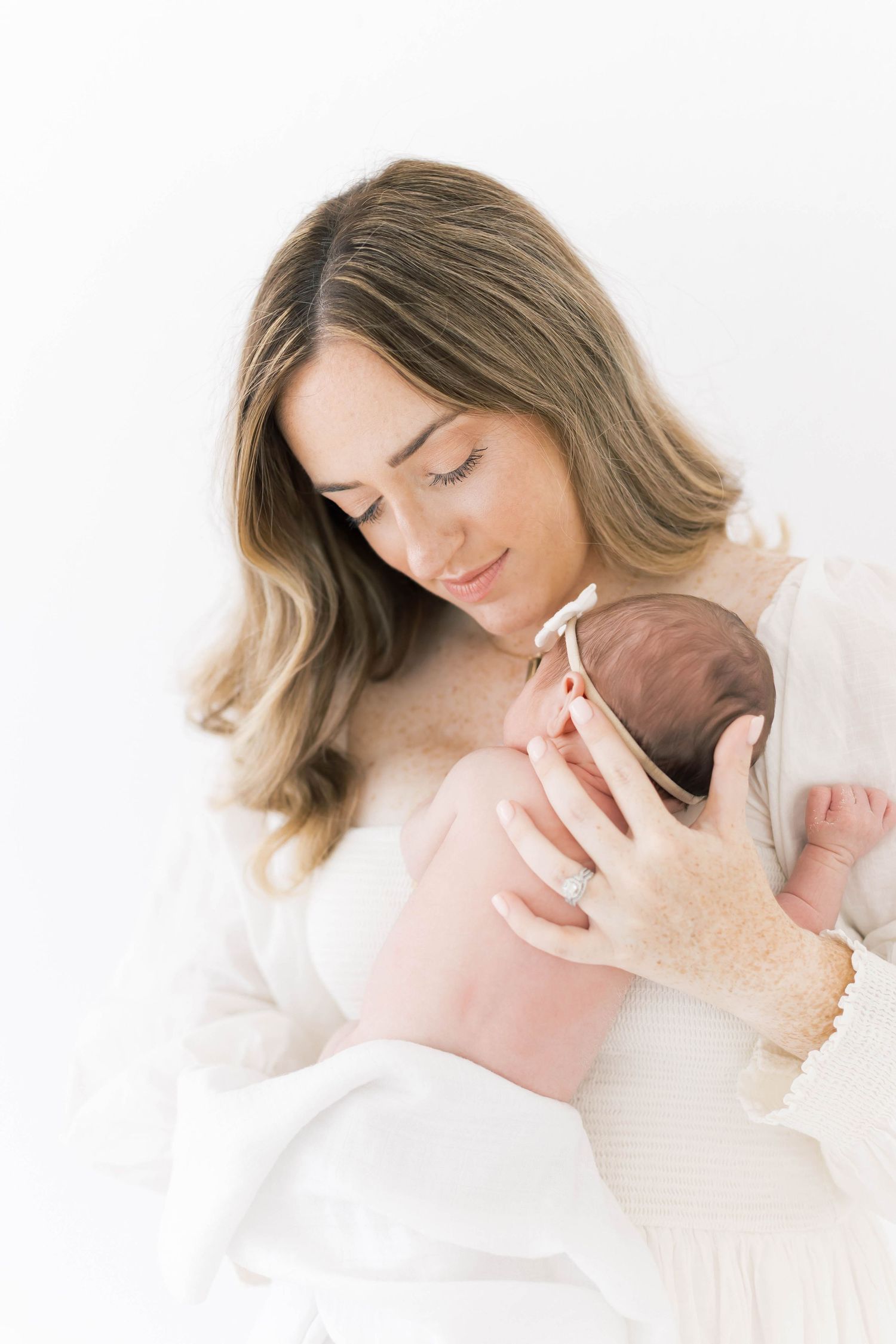 An intimate moment captured in soft lighting as a woman in white cradles a newborn.
