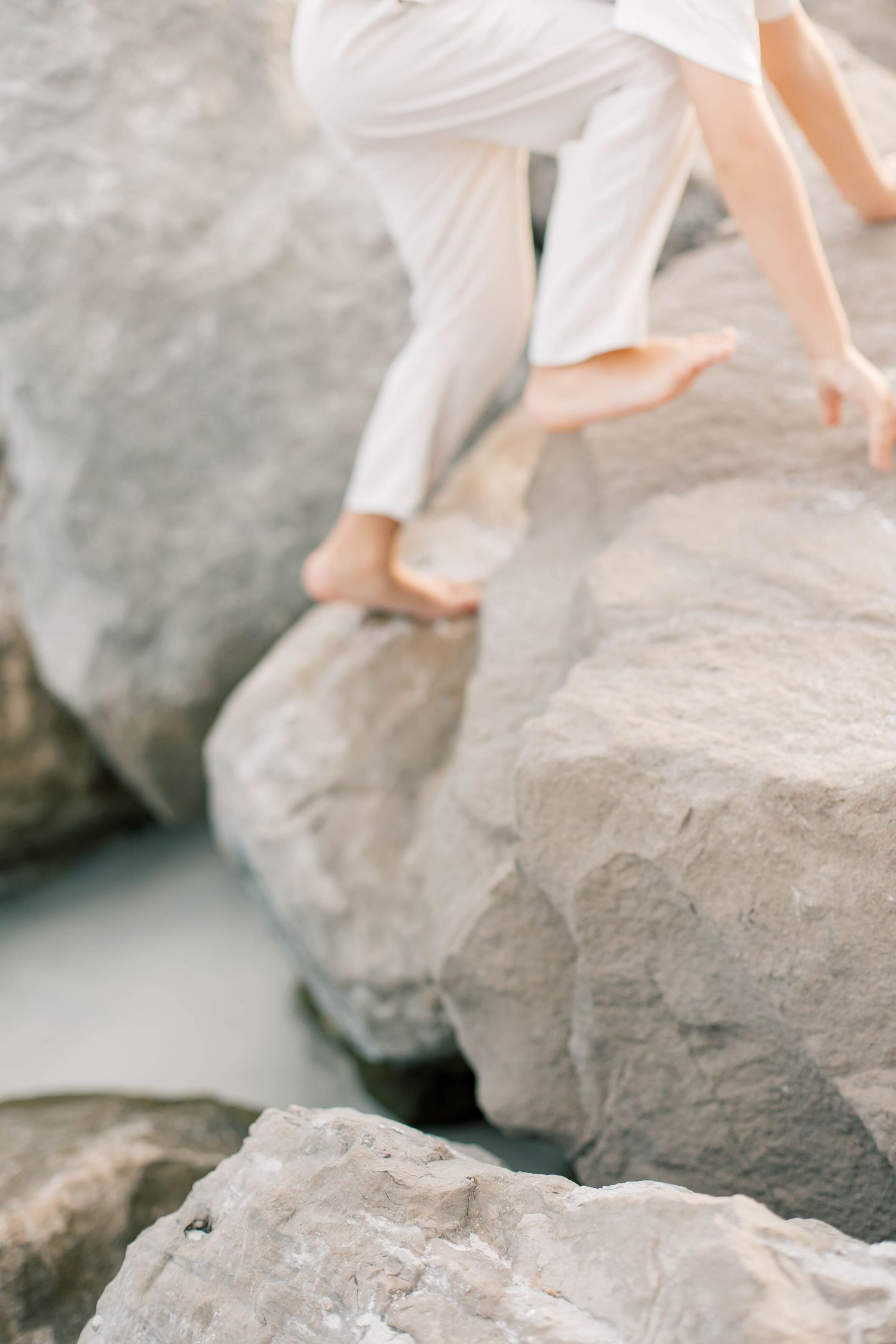 Feet and legs visible walking across large gray coastal rocks near the water.