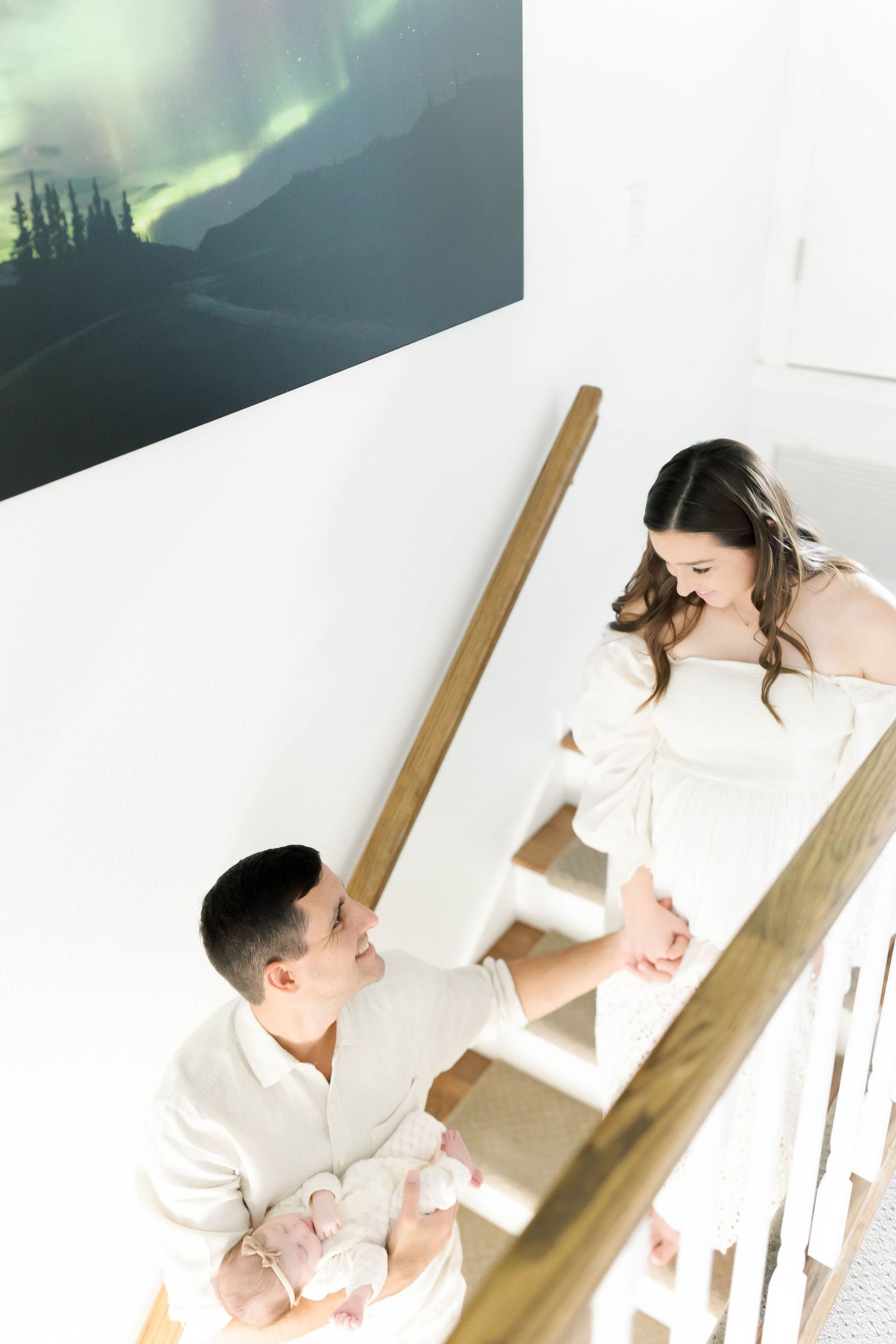 Parents on staircase with baby beneath aurora borealis artwork.