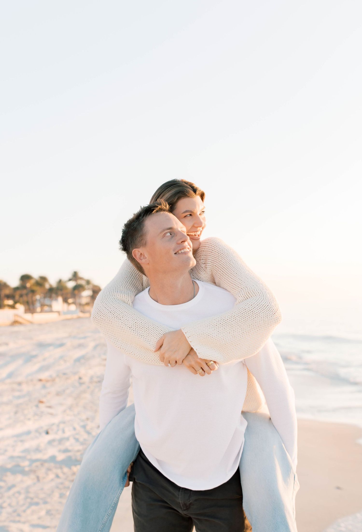 A playful piggyback ride on the beach with a couple in white and denim.