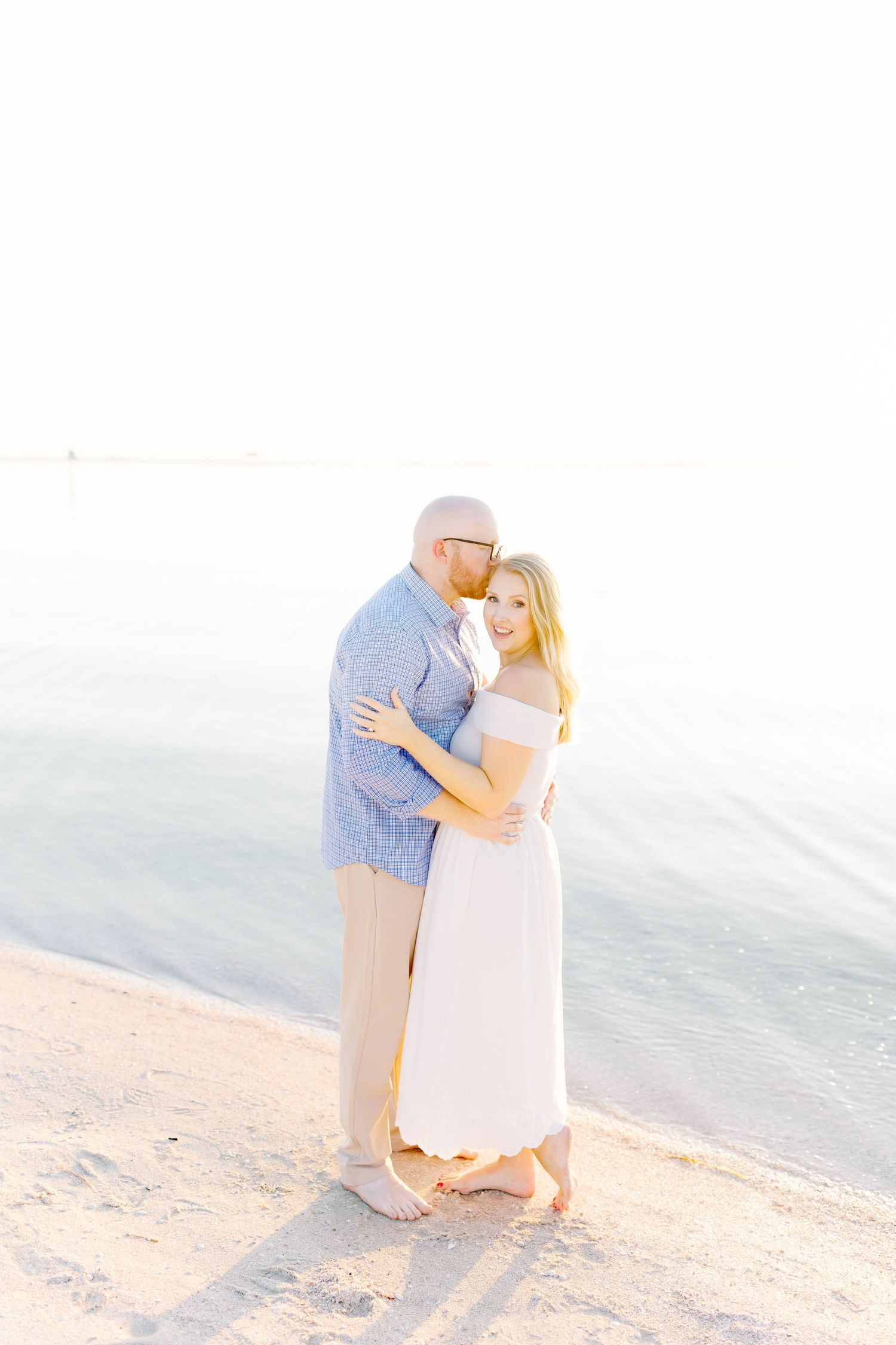 Romantic beach photoshoot with couple in white and blue attire against ocean backdrop.