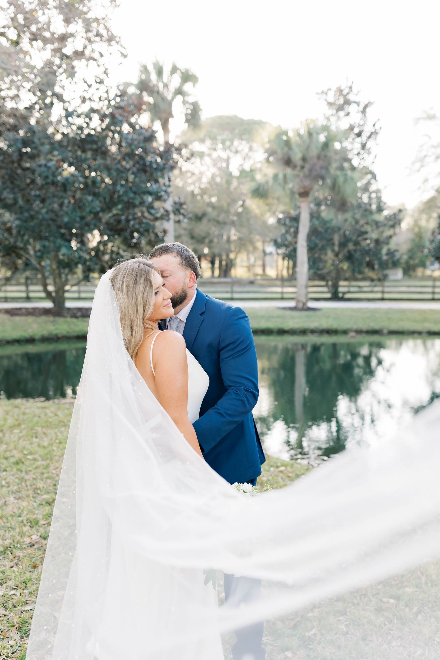 Flowing white veil catches breeze during lakeside wedding portrait.