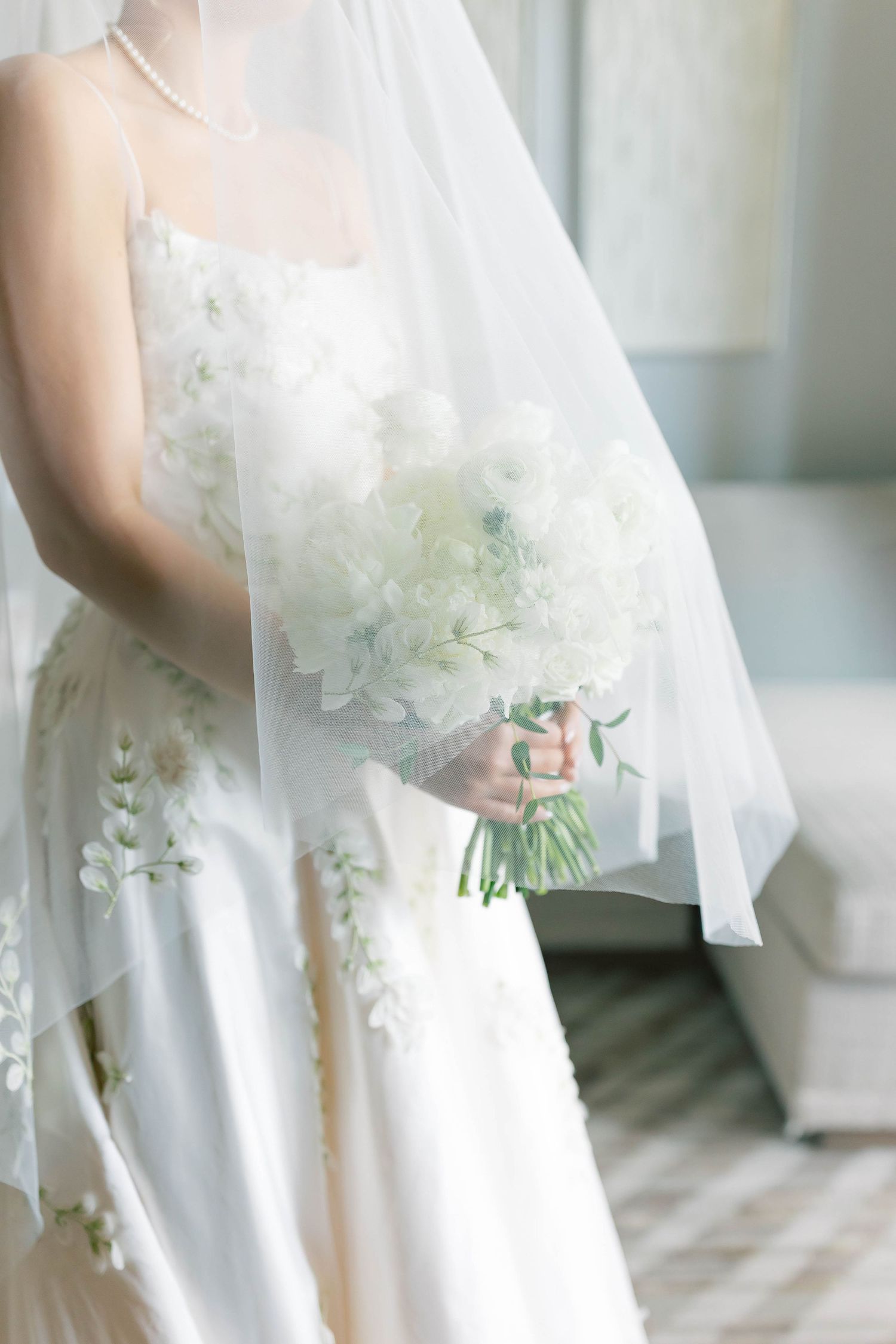 A delicate white wedding dress with floral details and veil is shown with a matching bouquet of white flowers.