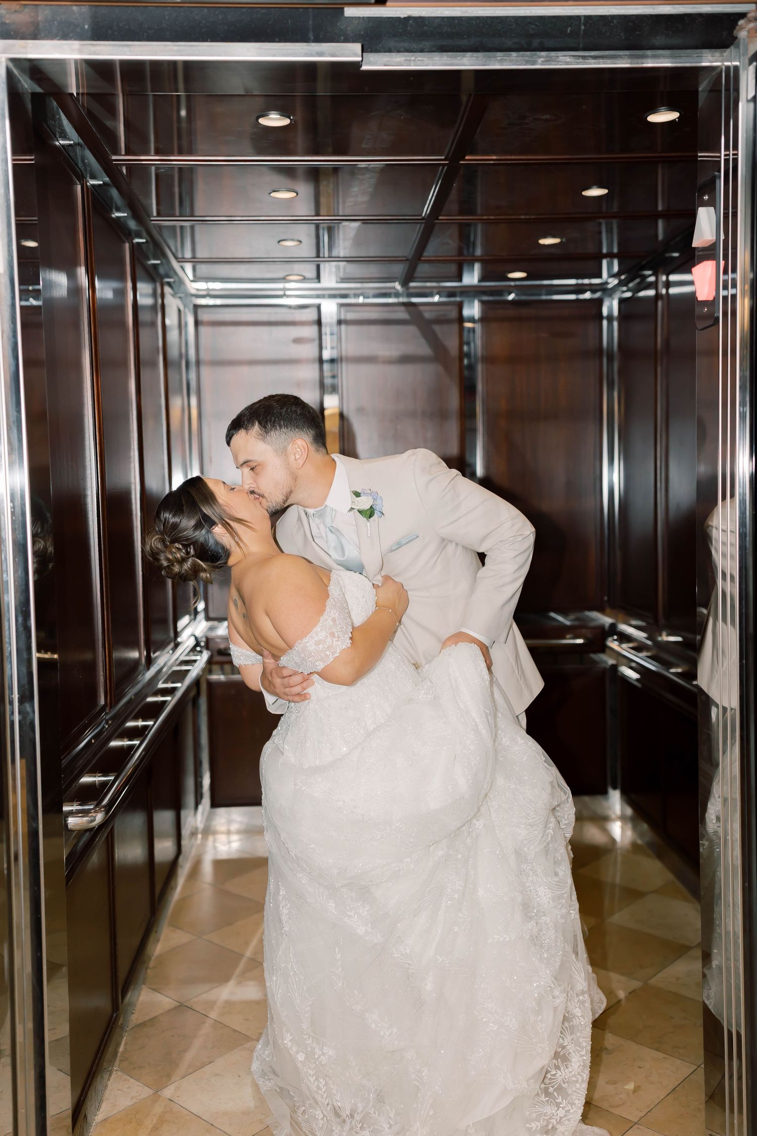 Bride and groom share a passionate kiss while dipping in a mirrored elevator on their wedding day.