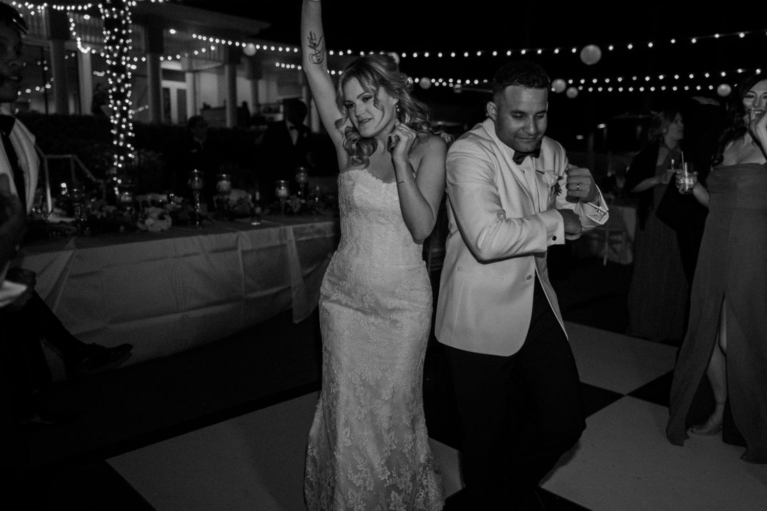 Wedding reception dance floor with string lights overhead and guests dancing in evening celebration.