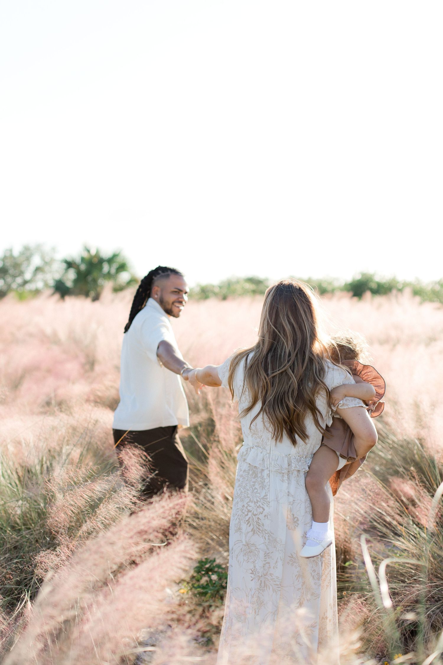 Couple dancing and embracing in a field of tall grass during golden hour.