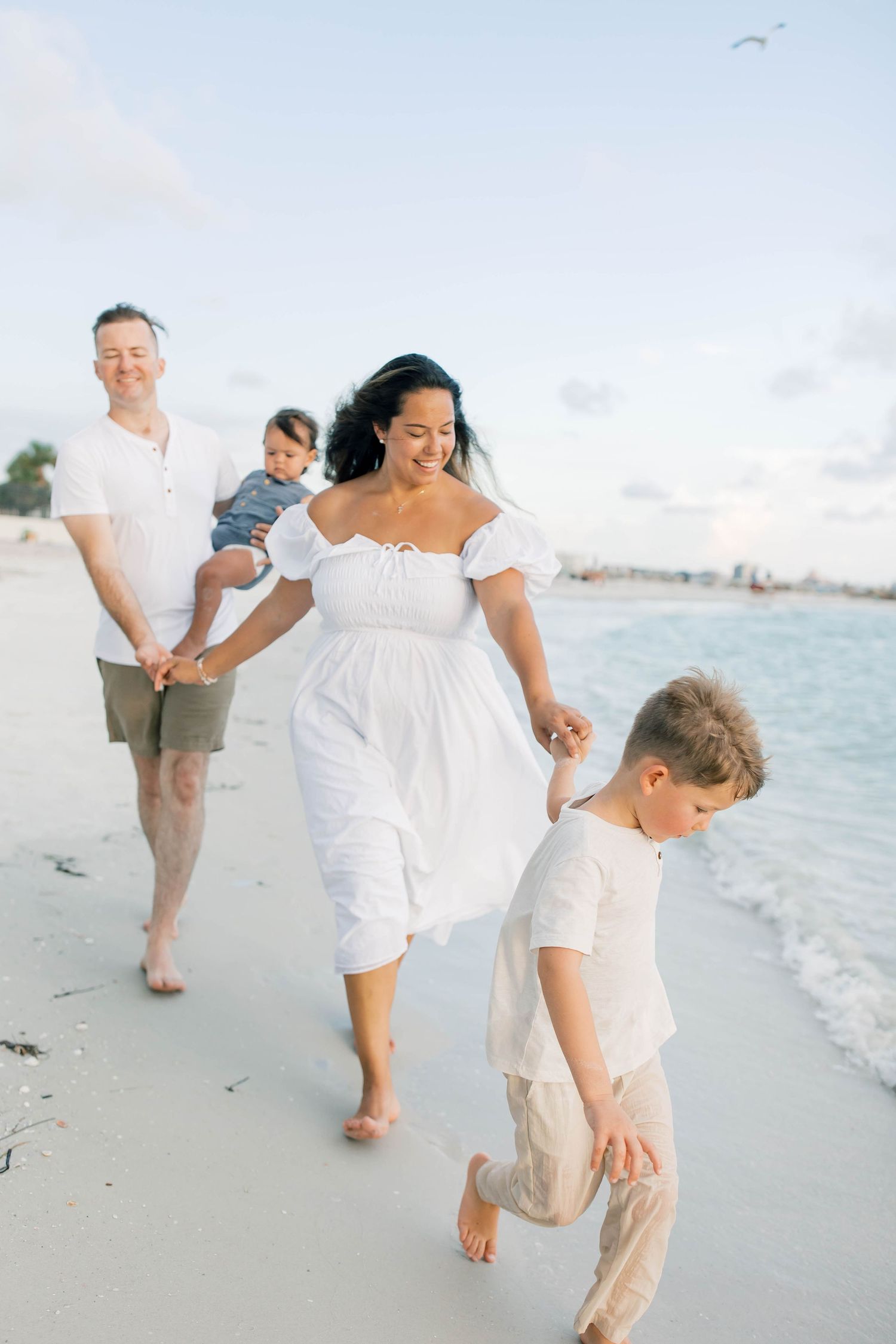 Family members walking and playing along the shoreline wearing white and beige outfits.