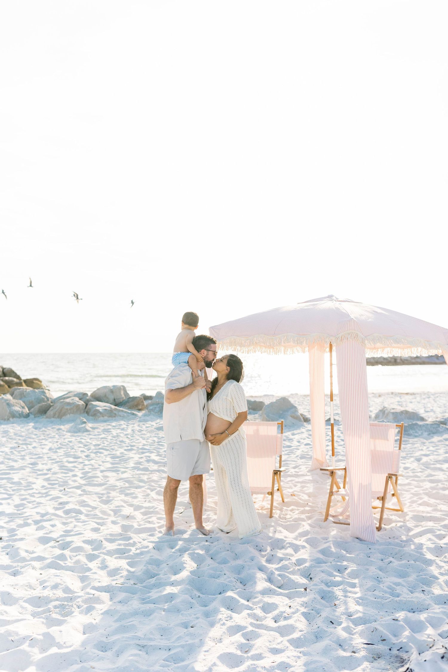 Romantic beach scene with white chairs and fabric canopy on pristine sand.