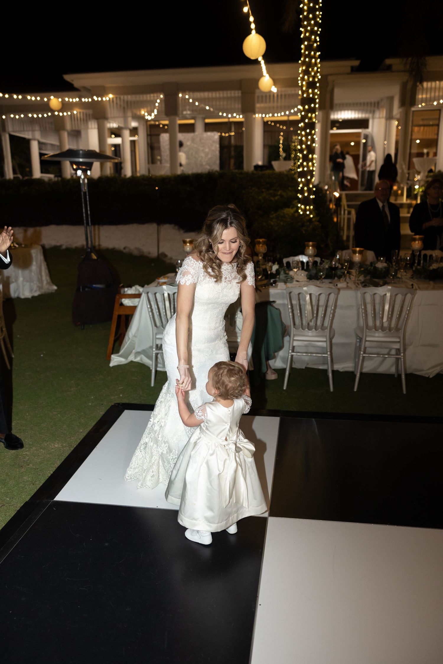 Young girls in white dresses dance together on a dance floor at an evening wedding reception.