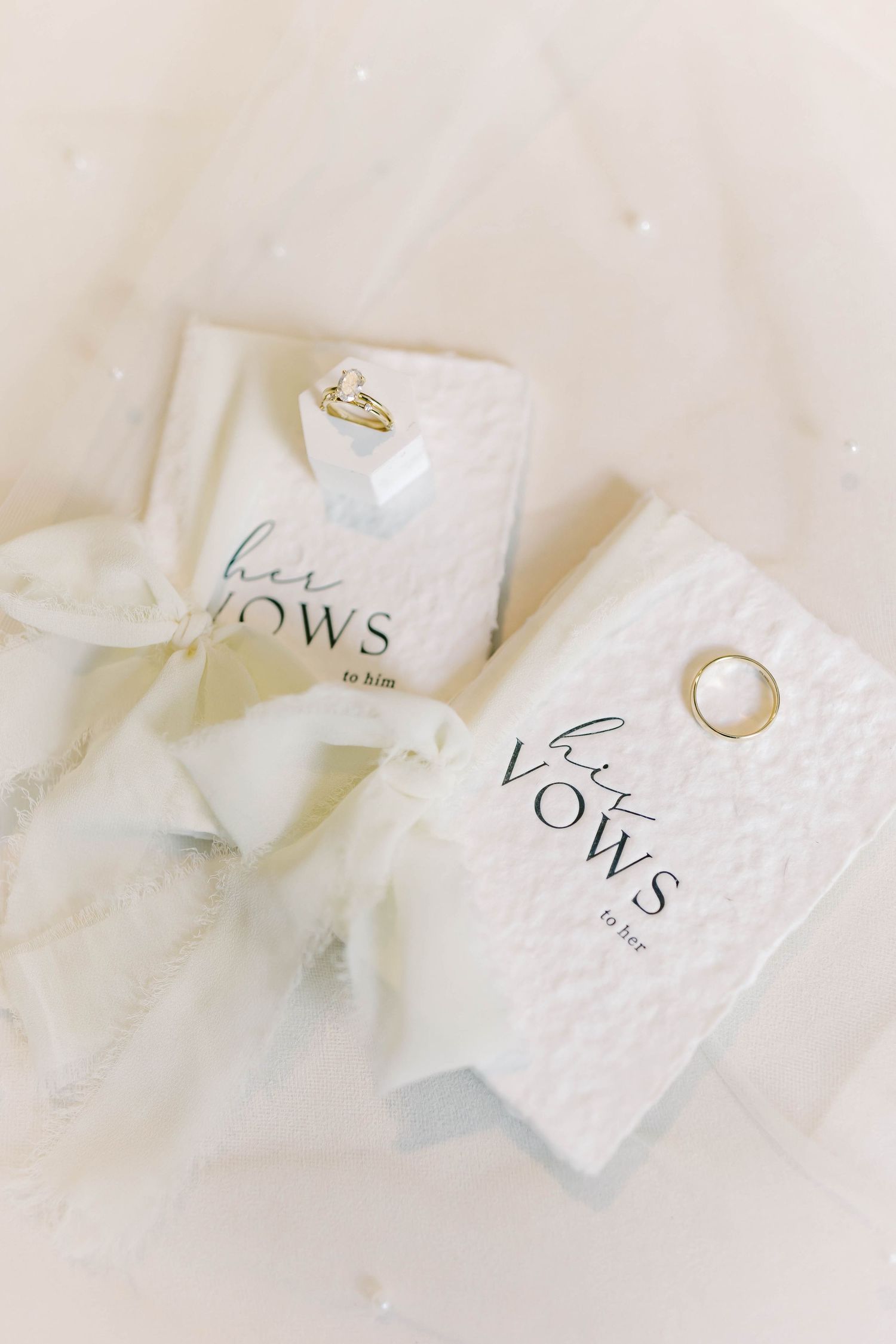 Wedding vow cards and rings arranged on white fabric.