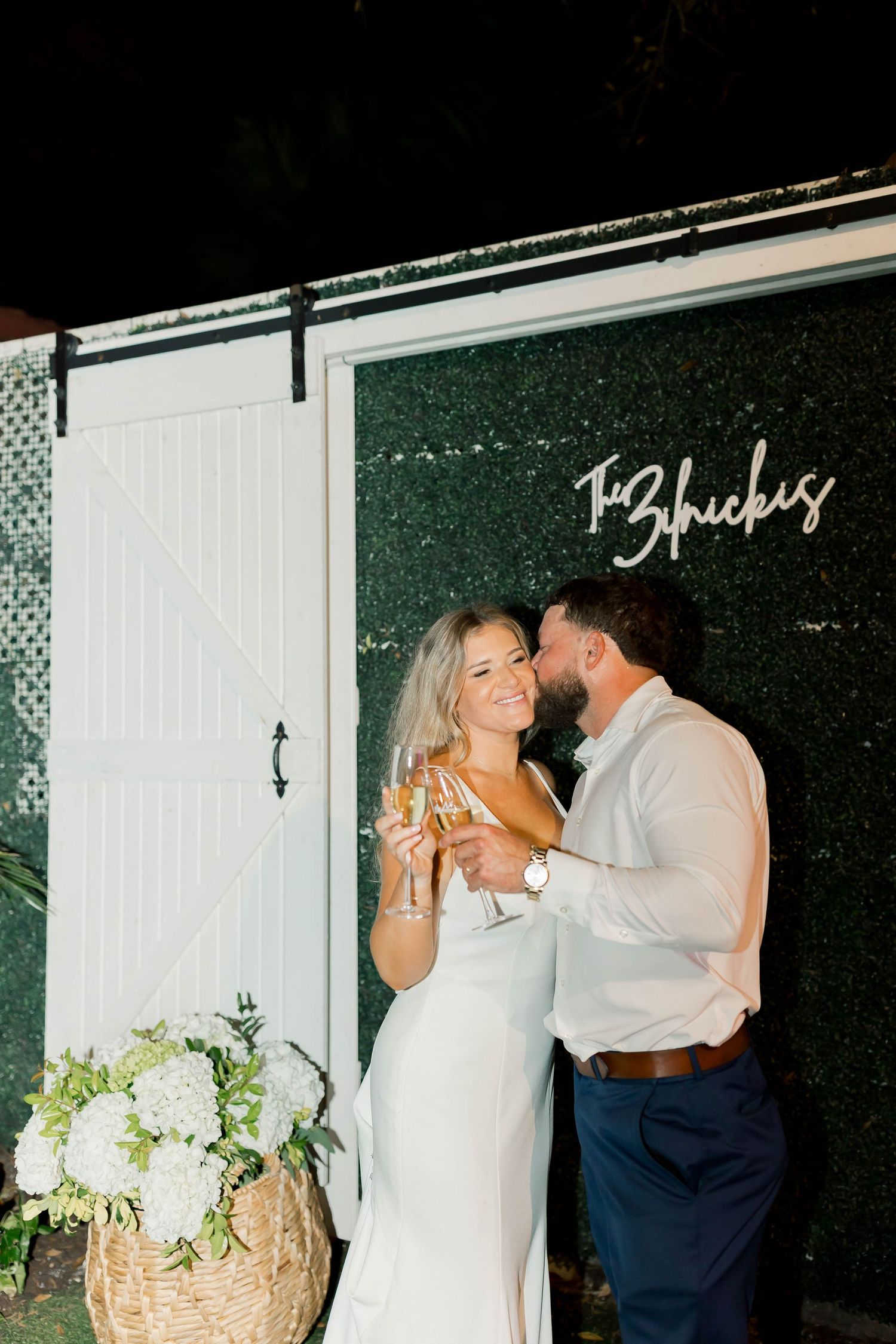 Newlyweds toasting with champagne against a greenery wall backdrop.
