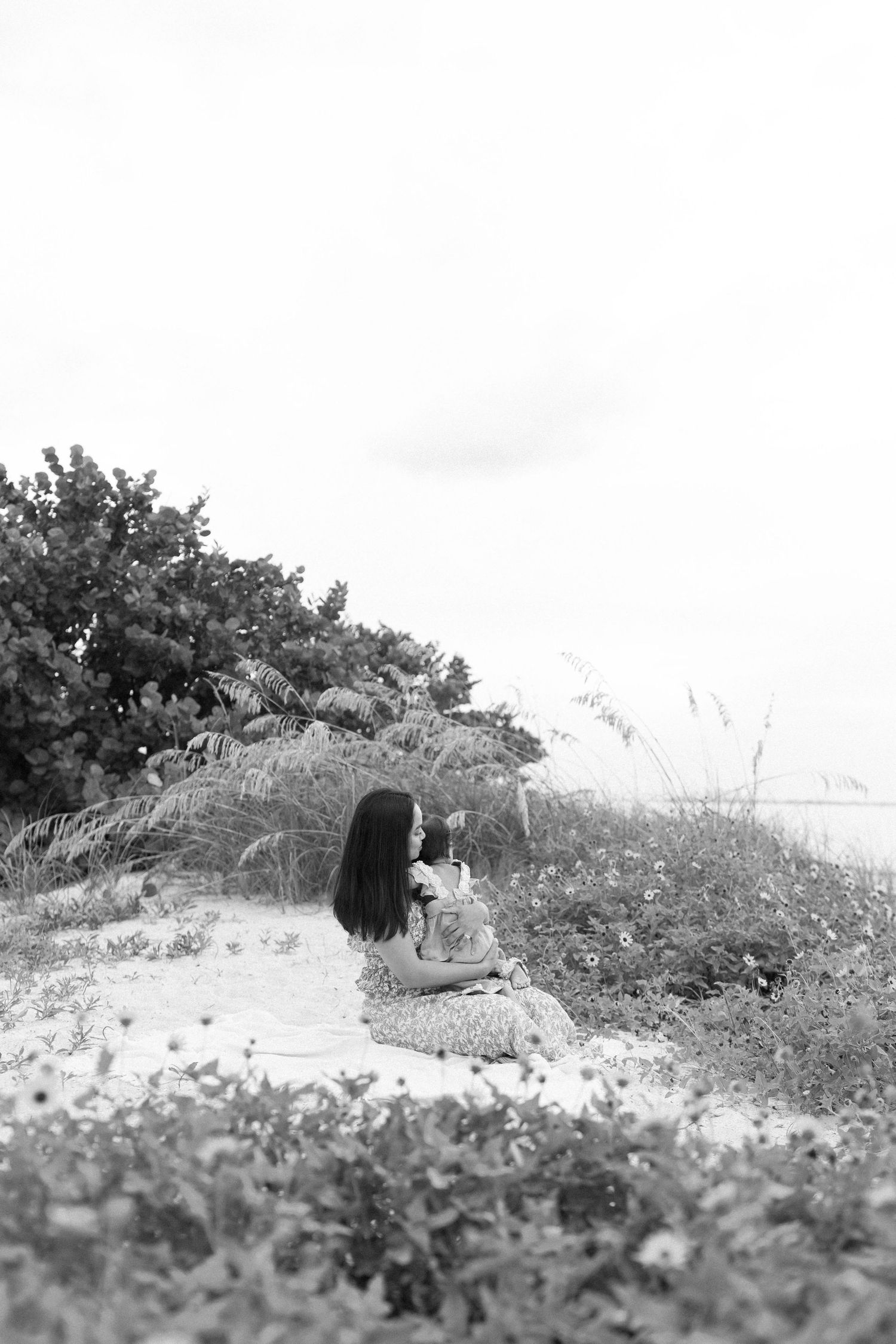 Black and white photo of someone sitting on a grassy hillside overlooking a scenic landscape.