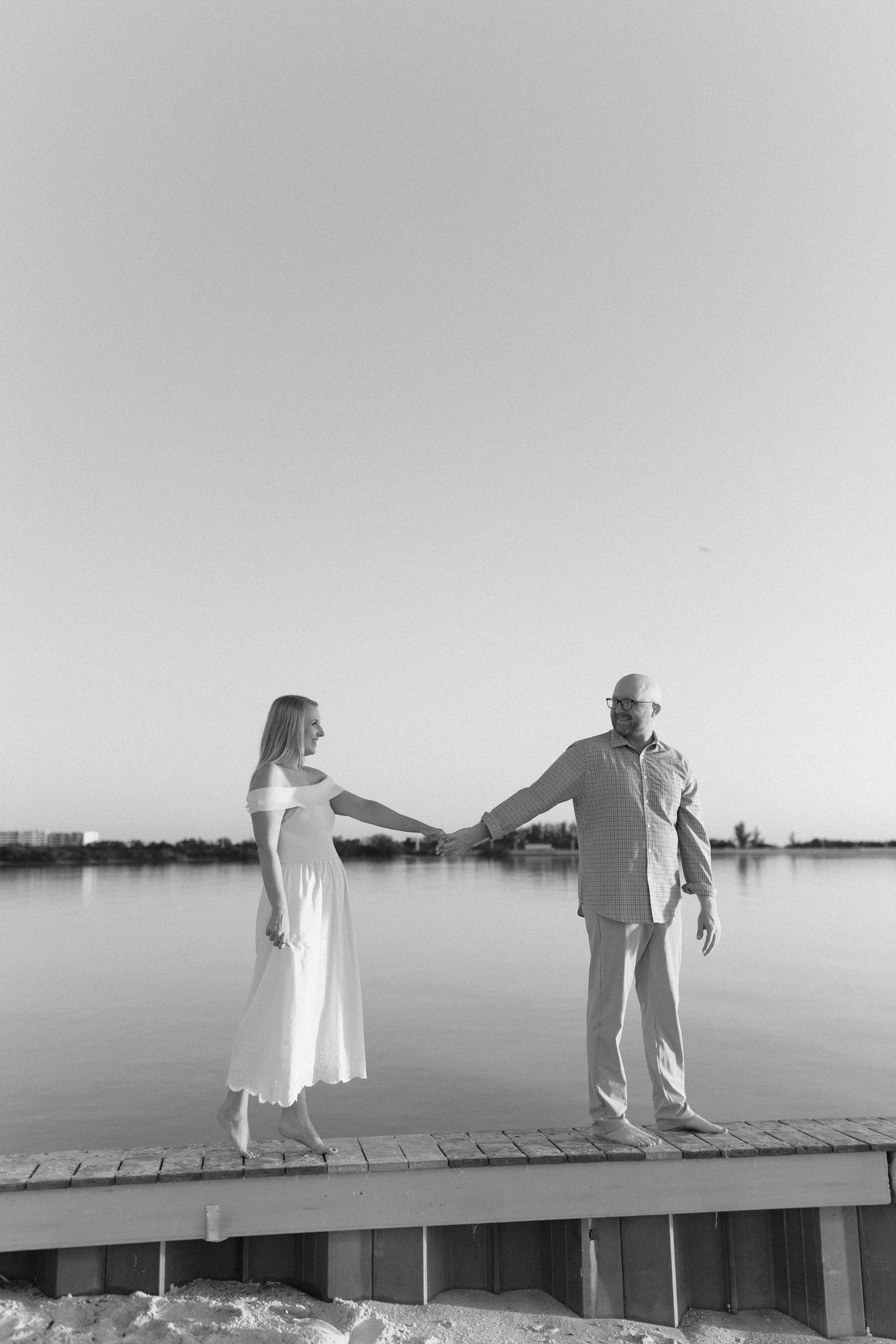 Playful couple posing on wooden dock by calm waters.