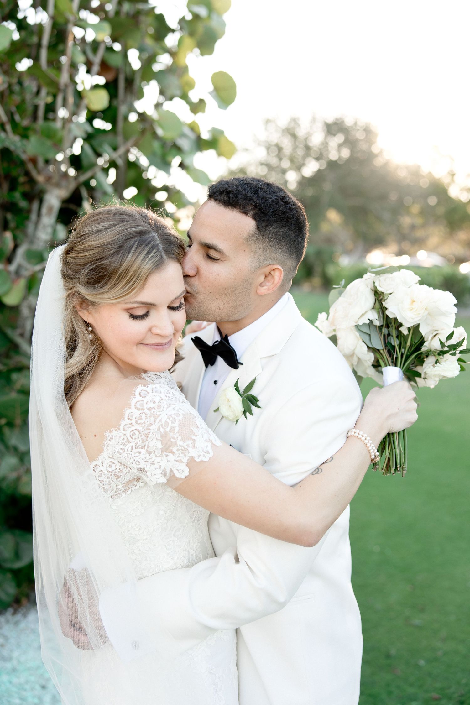 Romantic wedding portrait with white bouquet on lush green golf course at sunset.