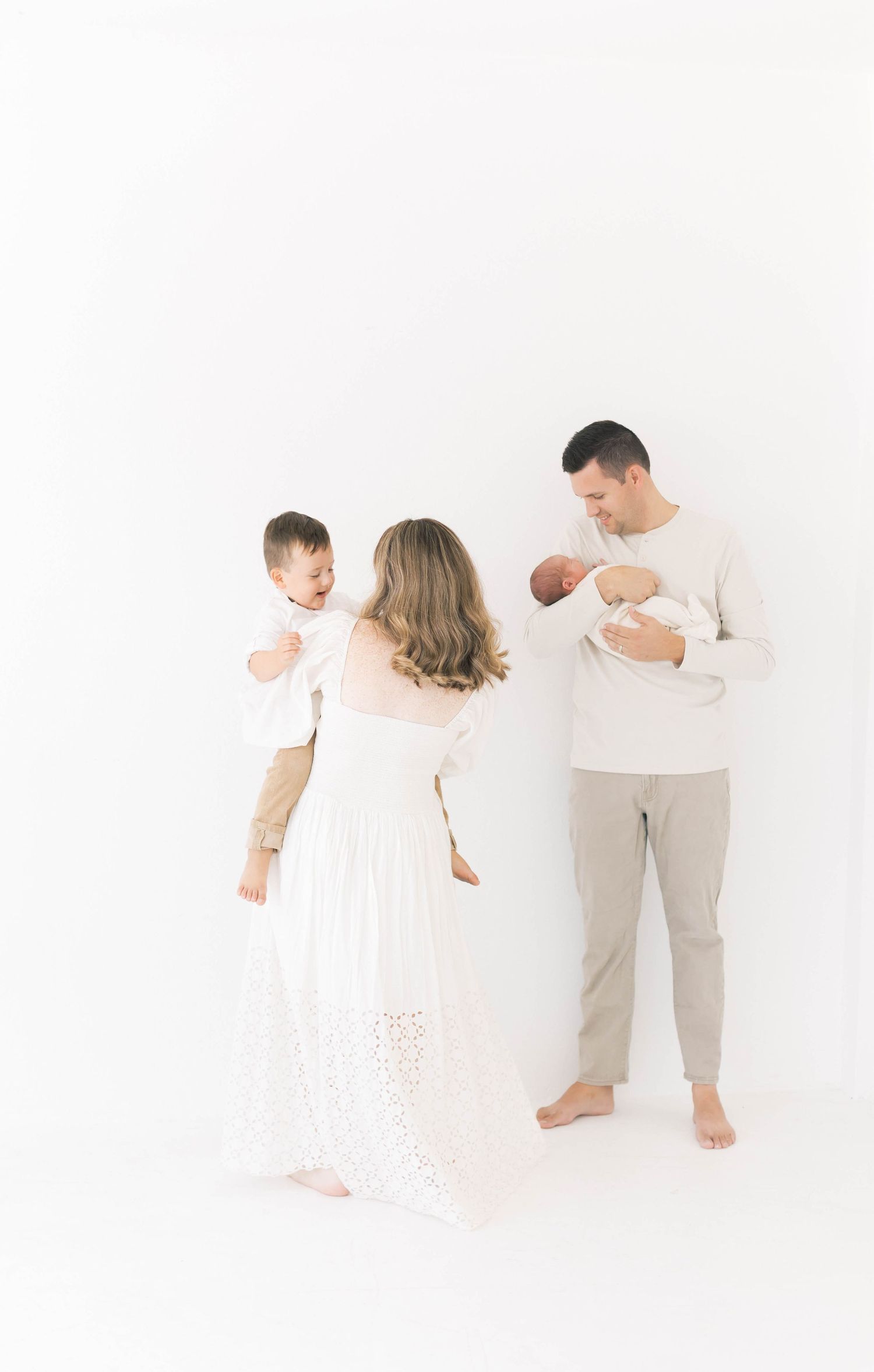 A family in white and beige clothing poses together against a bright white background.