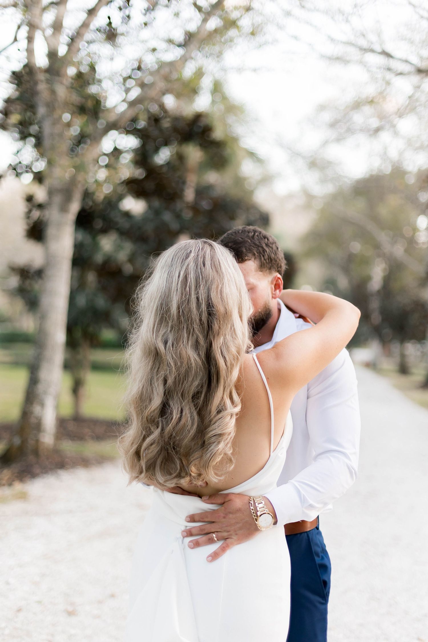 Intimate wedding portrait captured outdoors with soft natural lighting and trees in background.