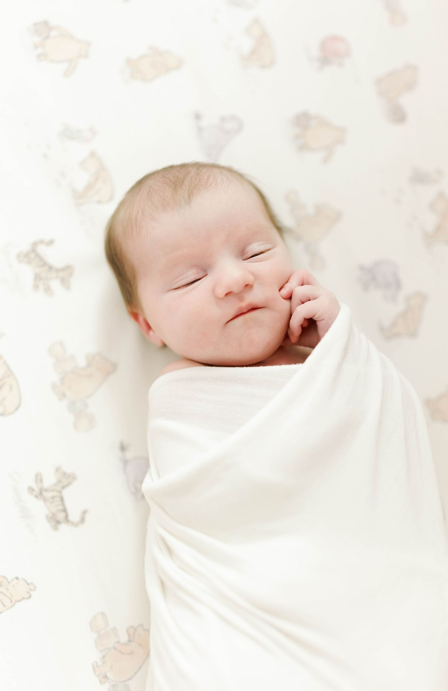 Peaceful sleeping newborn baby wrapped in soft white blanket against floral background.