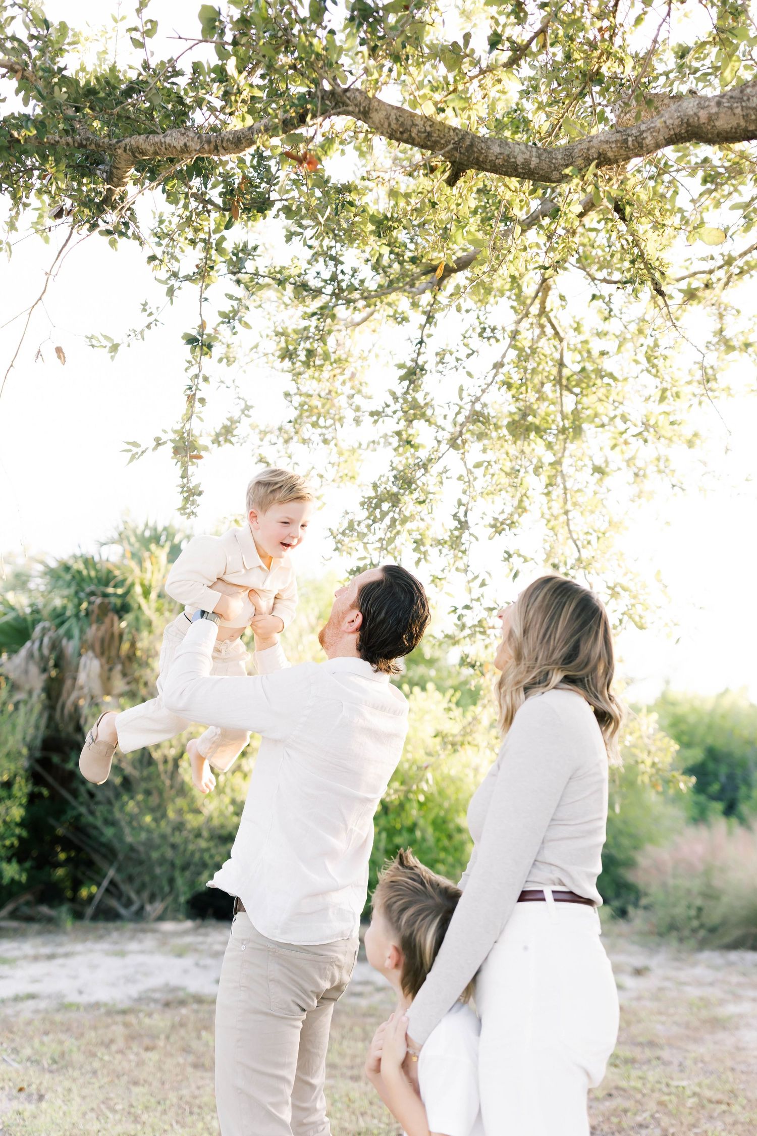 A family sharing playful moments under a sprawling tree branch in natural light.