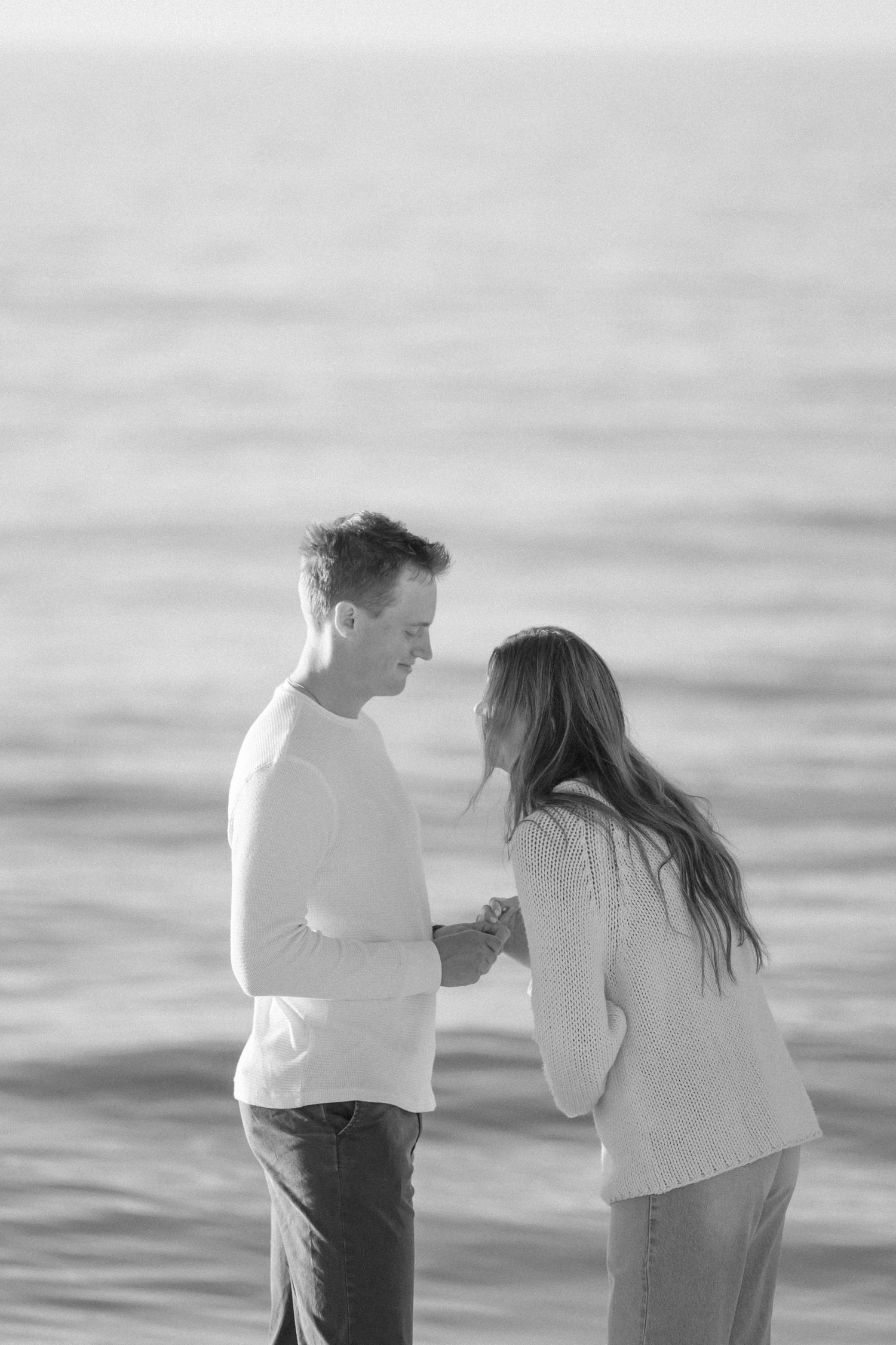 A romantic black and white beach scene shows two people sharing an intimate moment by the ocean.