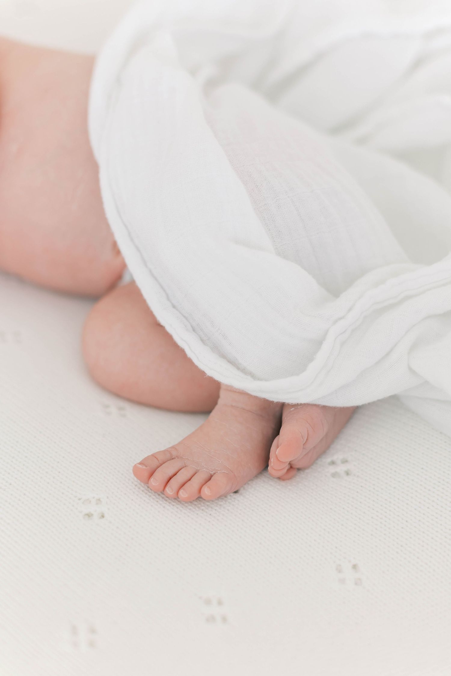 Tiny baby feet peek out from under a white blanket on a textured surface.