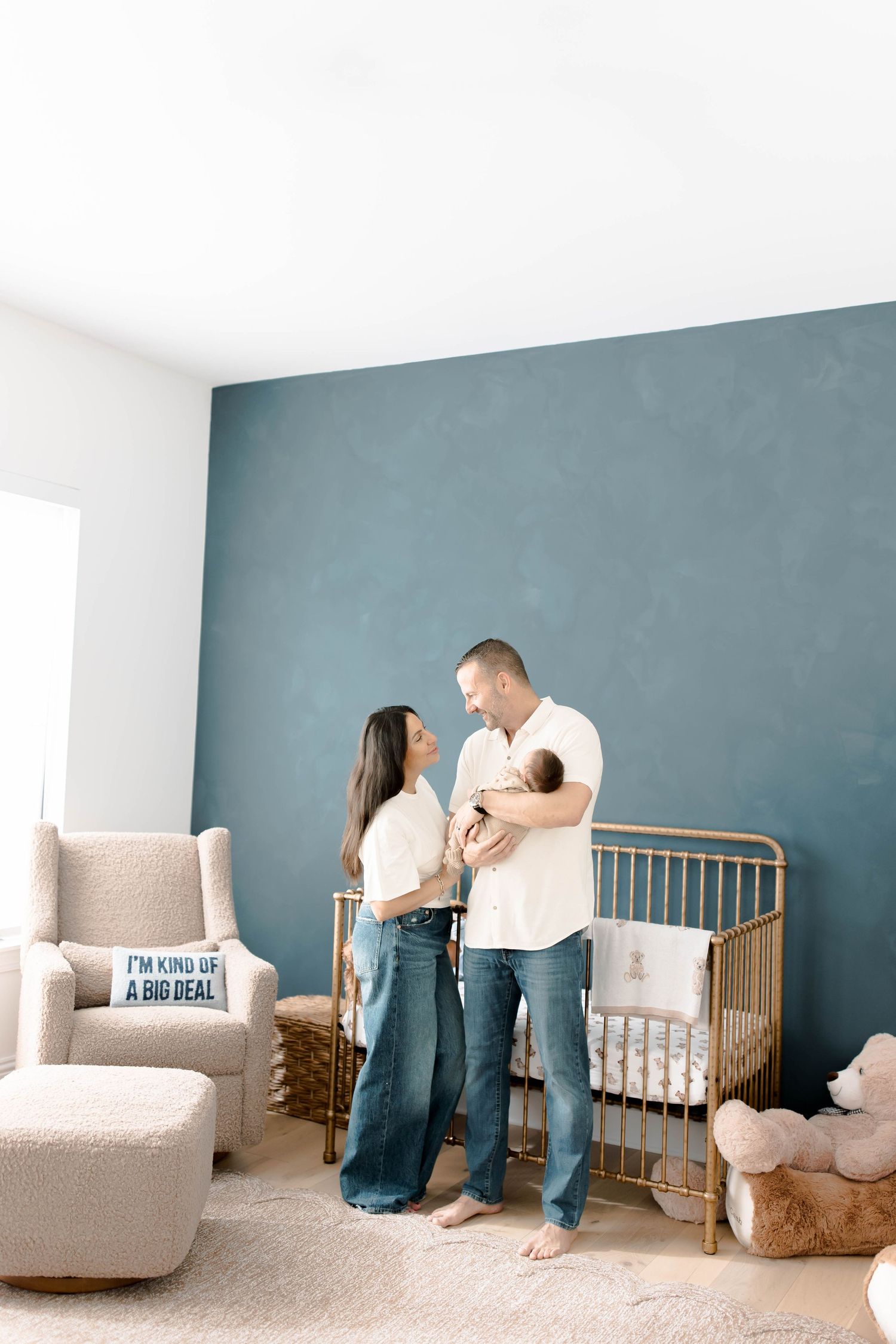 Couple standing together in nursery with blue accent wall and wooden crib.