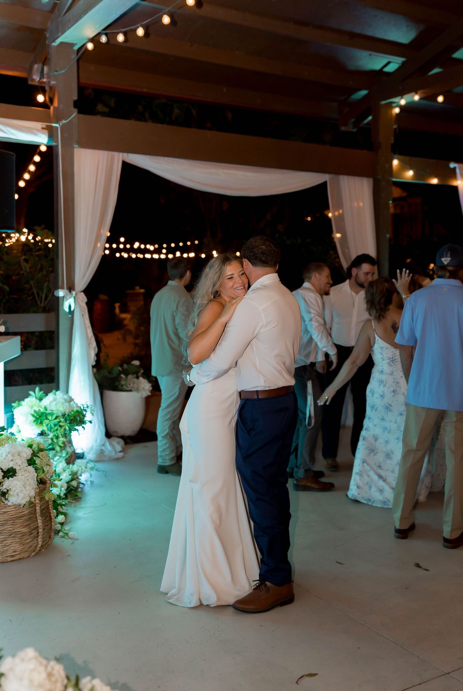 Couple sharing an intimate dance moment under string lights and white drapes at their wedding reception.