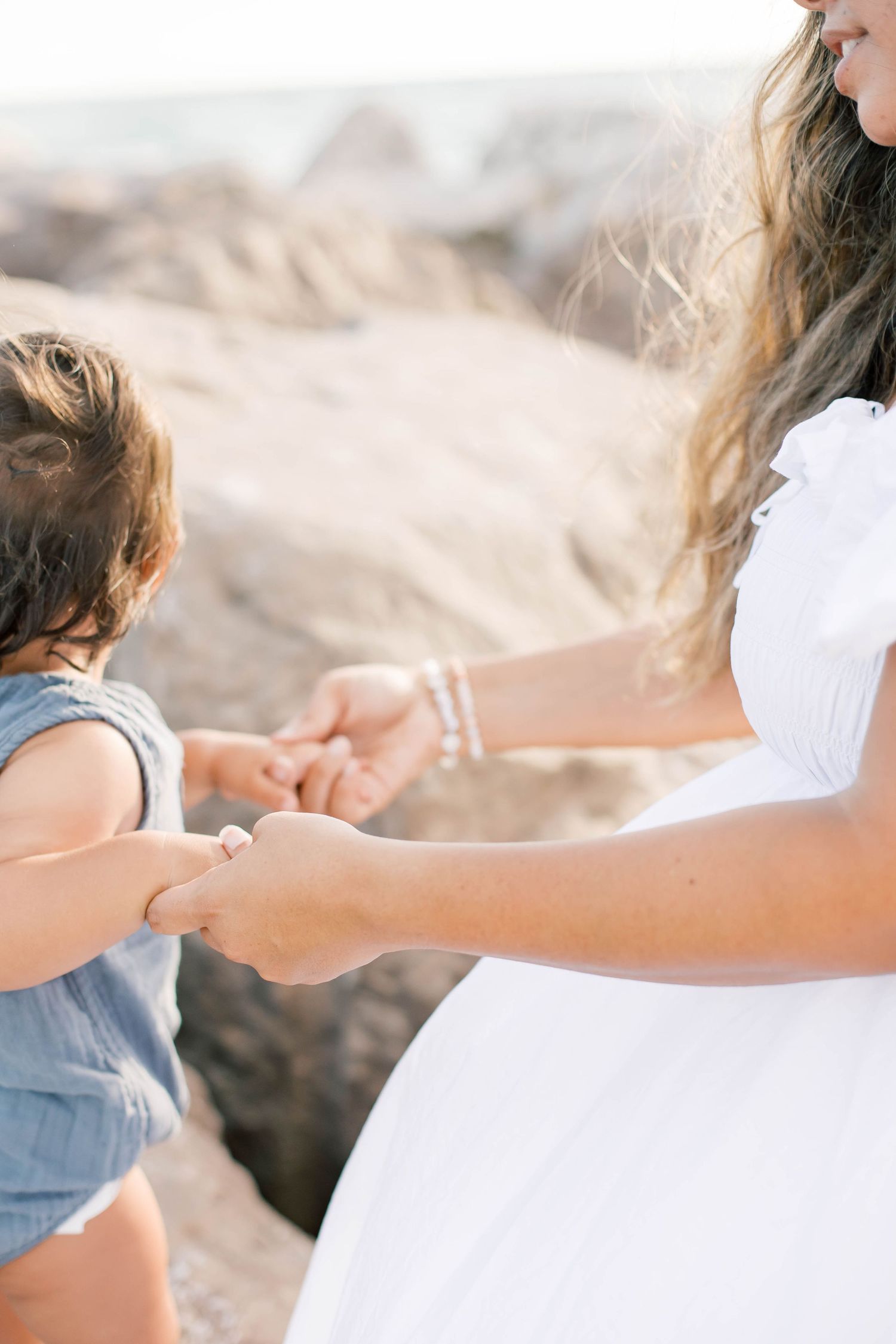 Delicate details of hands reaching and connecting on a sunny beach.