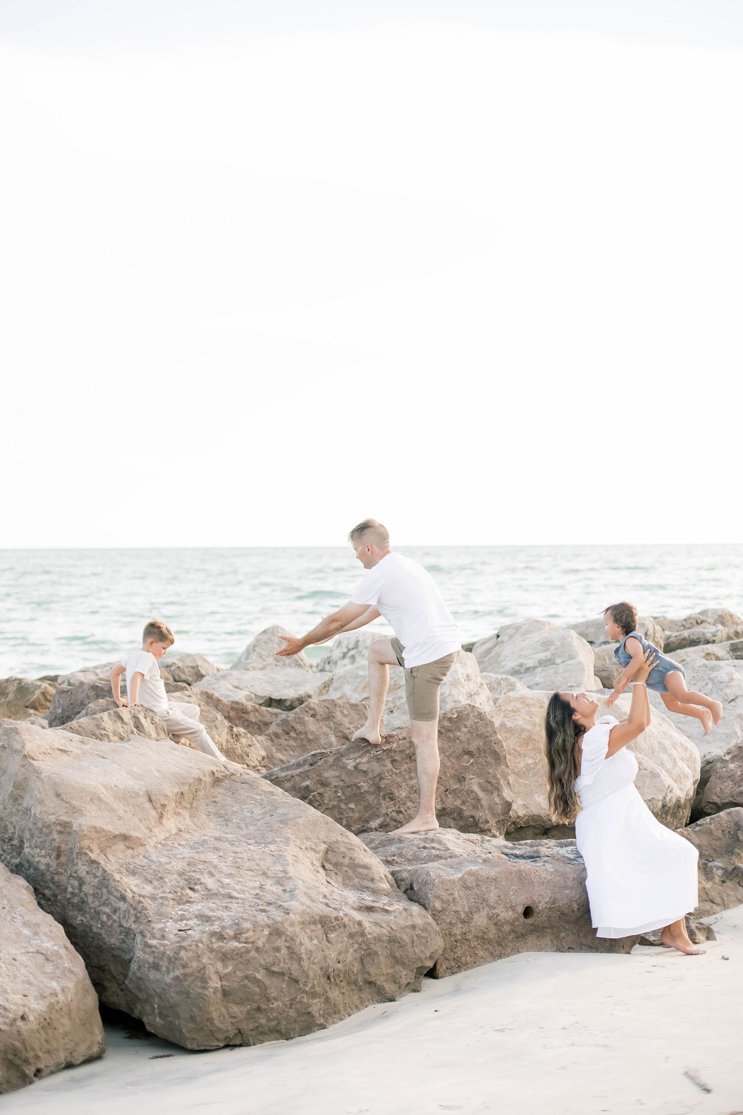 A sweet family moment captured on a bright beach with coastal rocks.