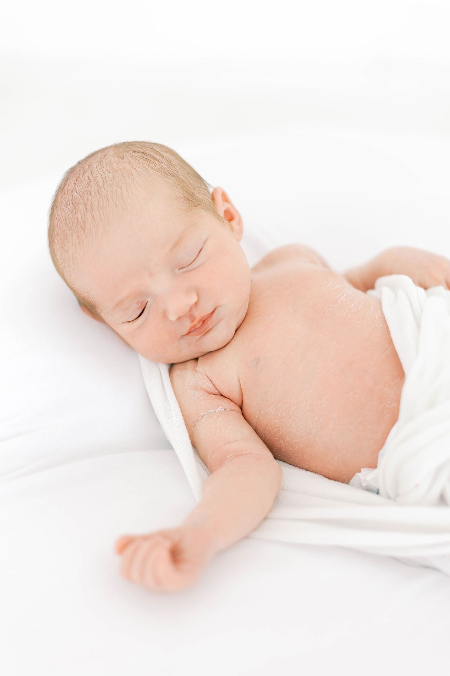 Serene newborn baby sleeping peacefully on white bedding.