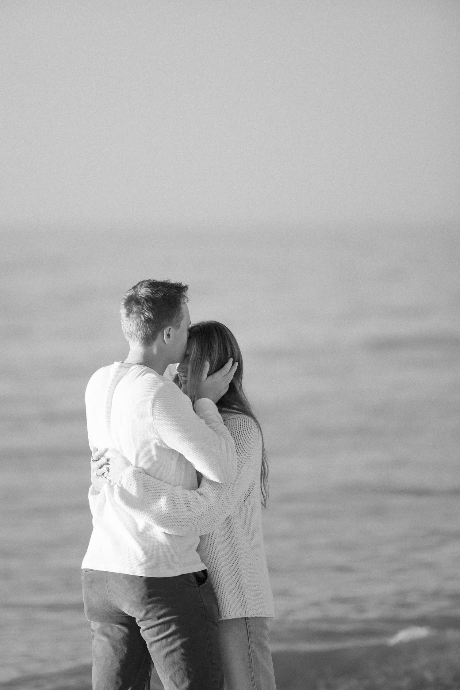 A black and white photograph captures an emotional embrace on the beach.