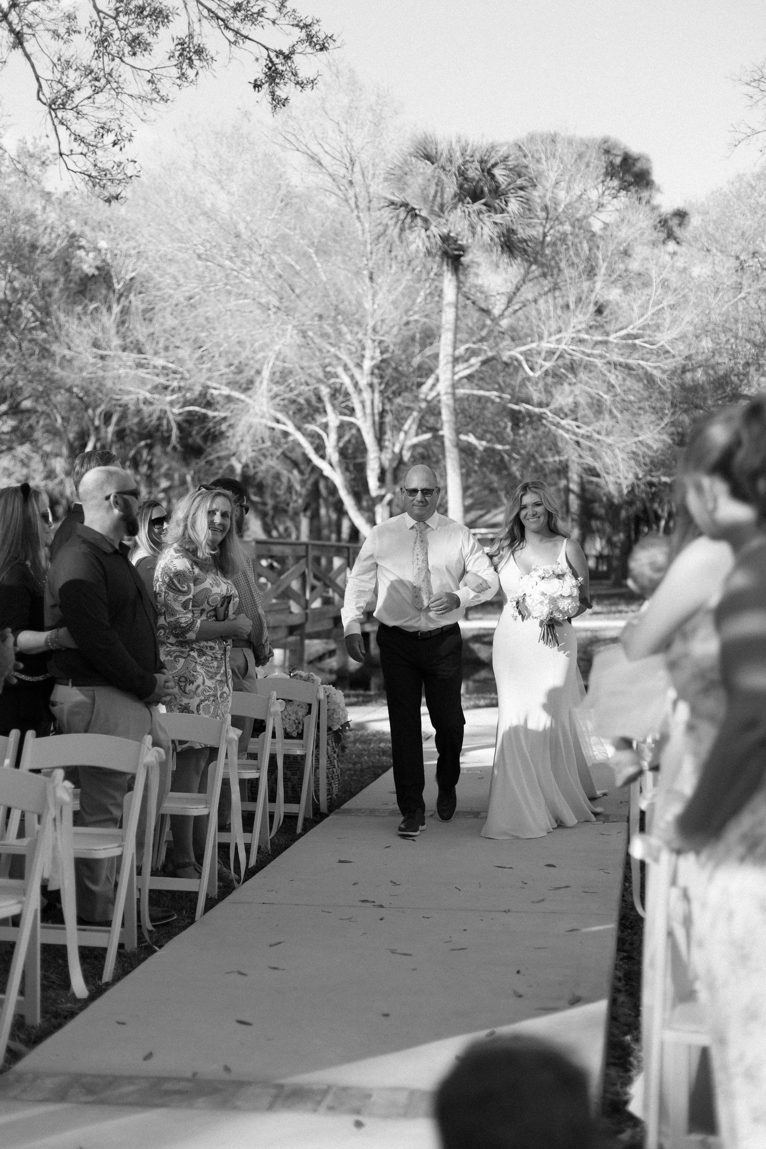 Wedding ceremony guests seated in white chairs during an outdoor celebration.