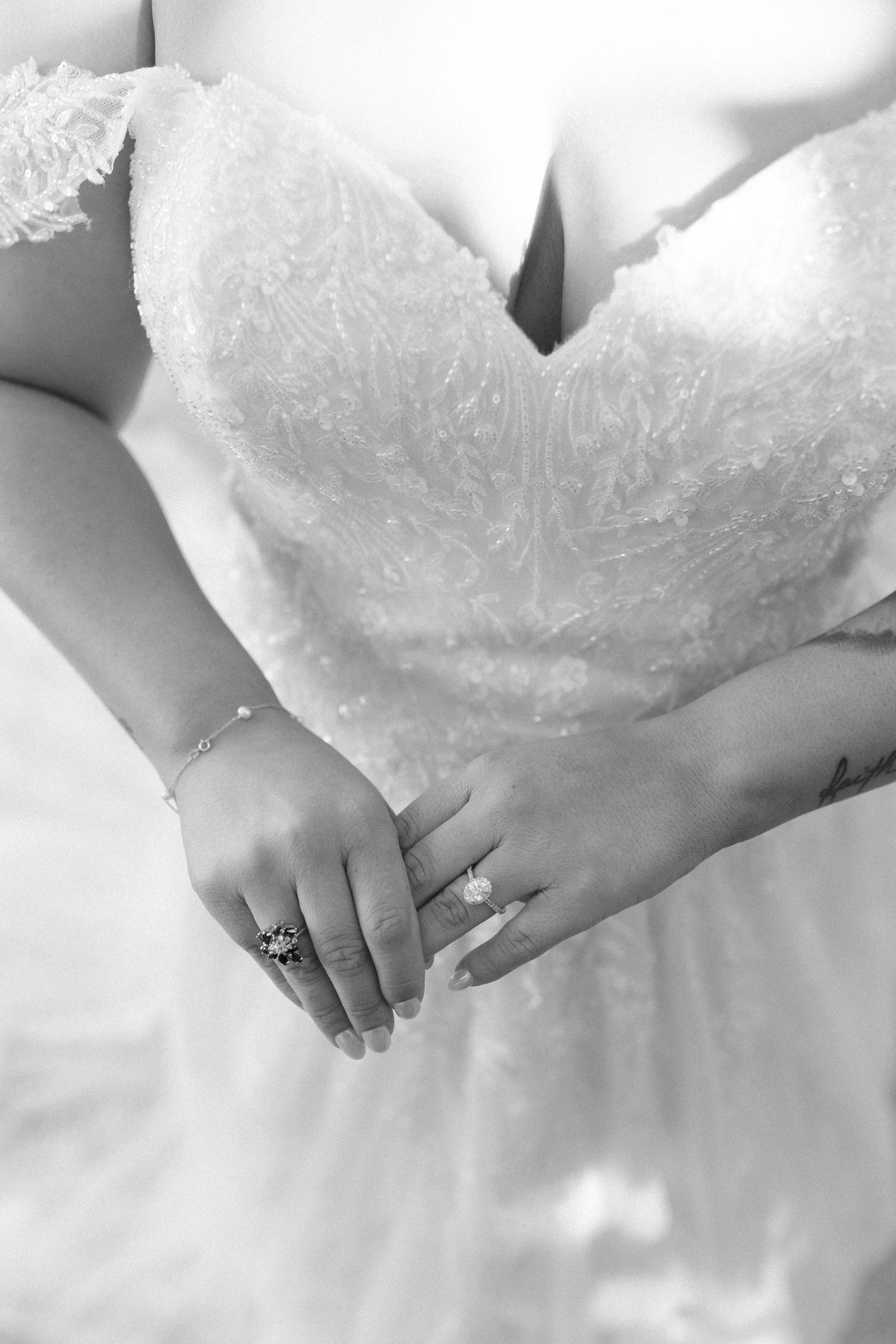 Close-up black and white photo of bride's hands clasped together wearing elegant rings and delicate bracelet.