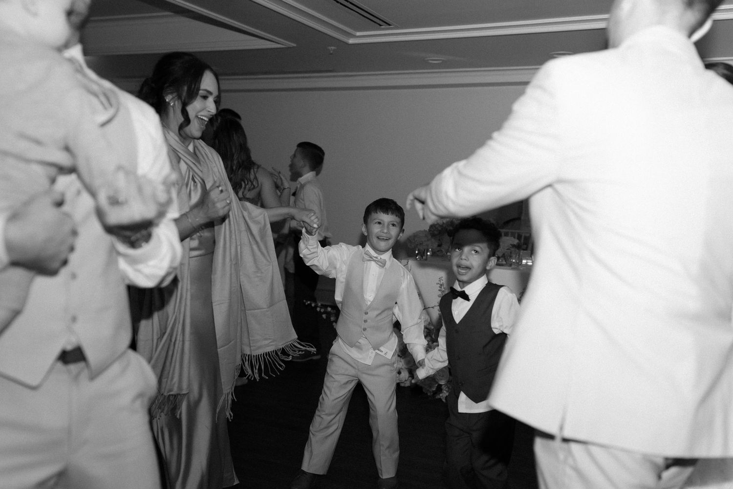 Black and white photo of guests dancing joyfully at a lively wedding reception celebration.