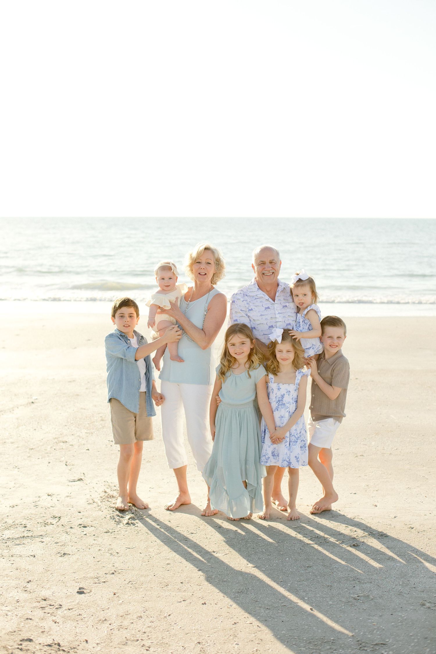Family group poses together on sunny beach in coordinated blue and white outfits.