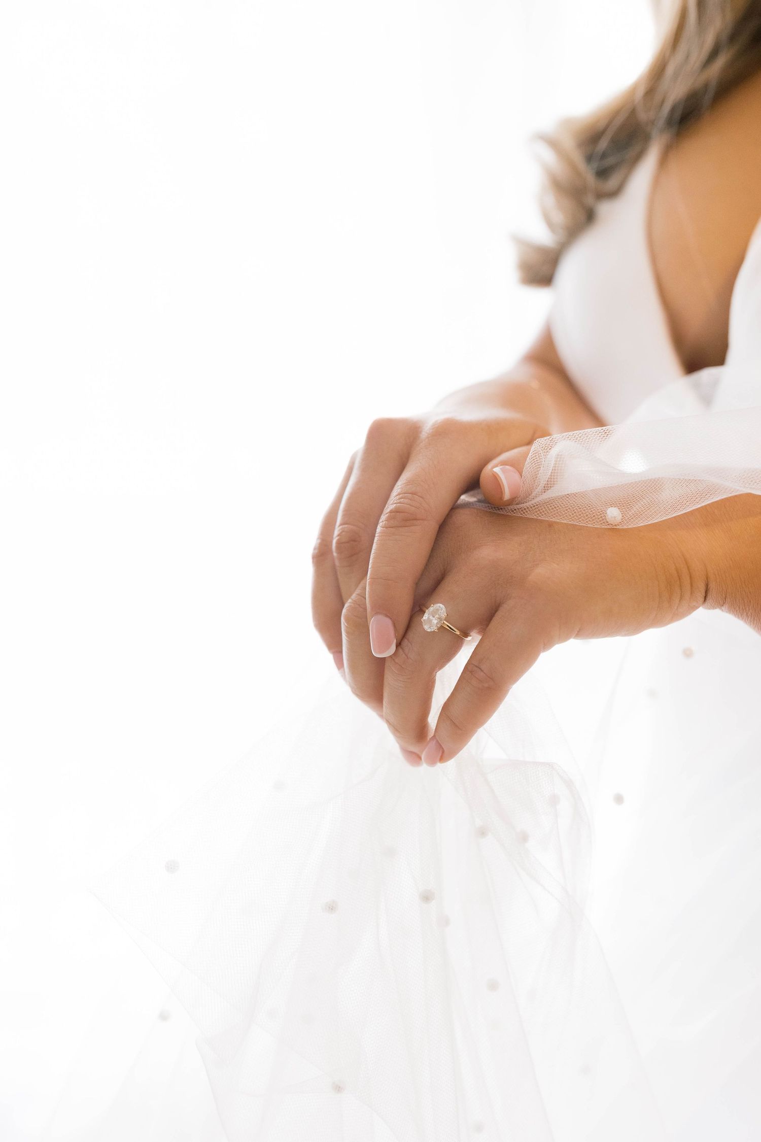 Close-up of hands adjusting a white wedding dress in natural light.