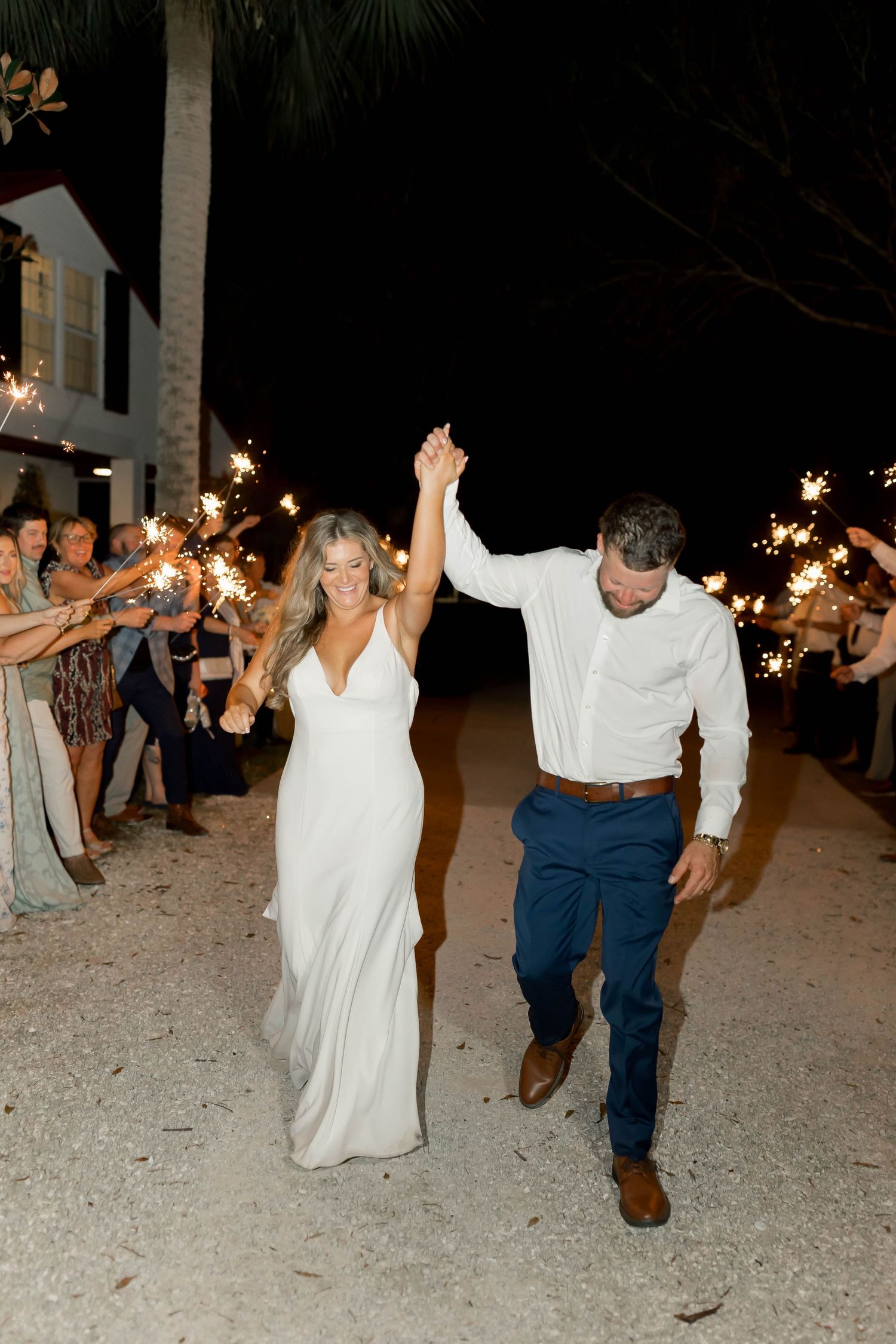 Couple making grand exit through sparkler tunnel at night.