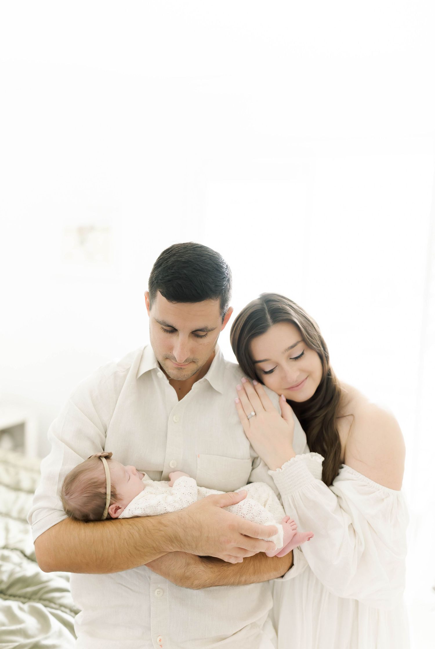 Family shares tender moment with newborn baby in bright minimalist setting.