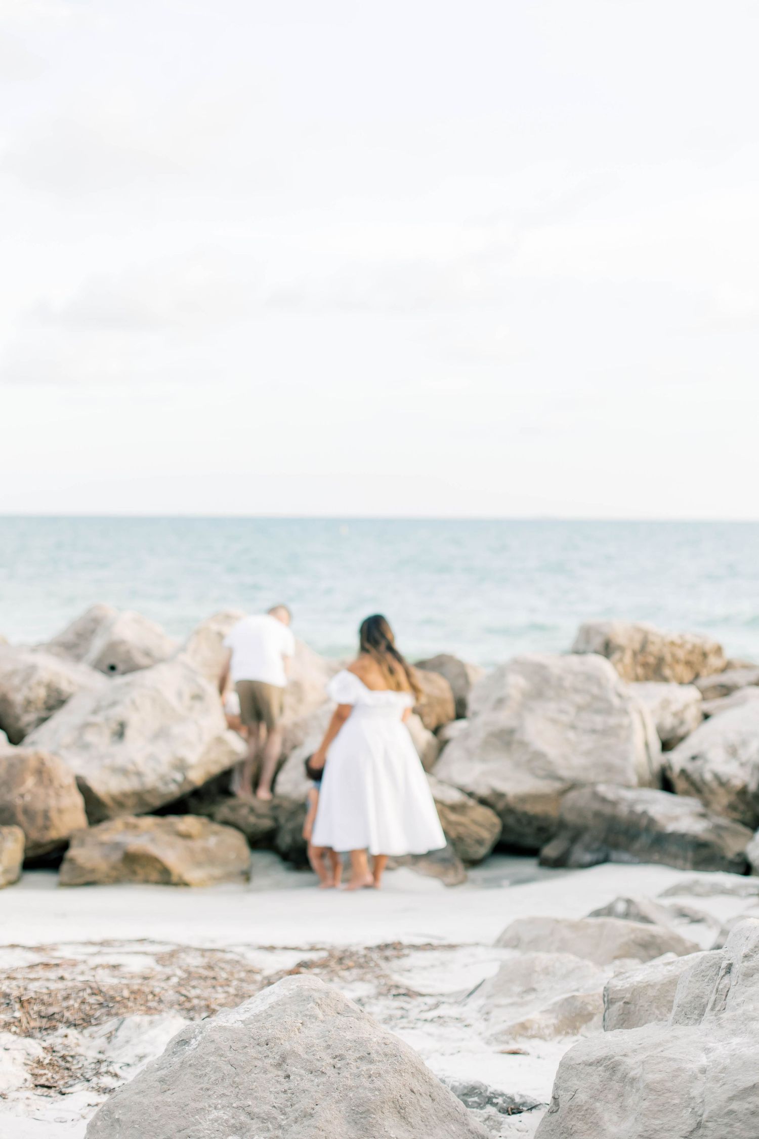 A serene beach scene with large rocks and people in white clothing by the water.